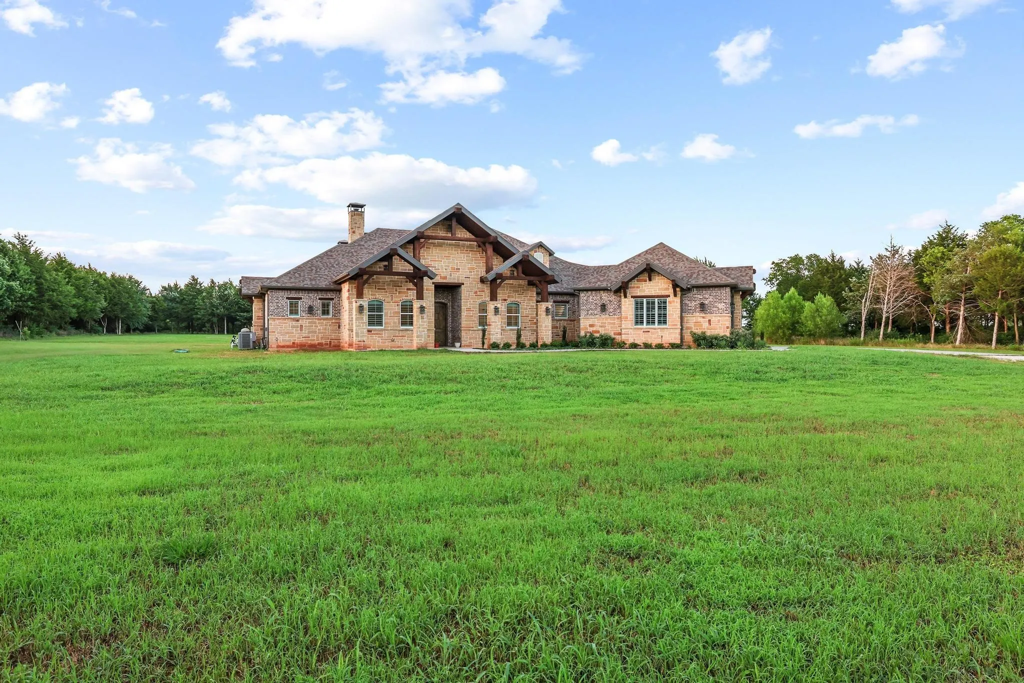Expansive green lawn presenting a stone and brick exterior with a prominent front entrance