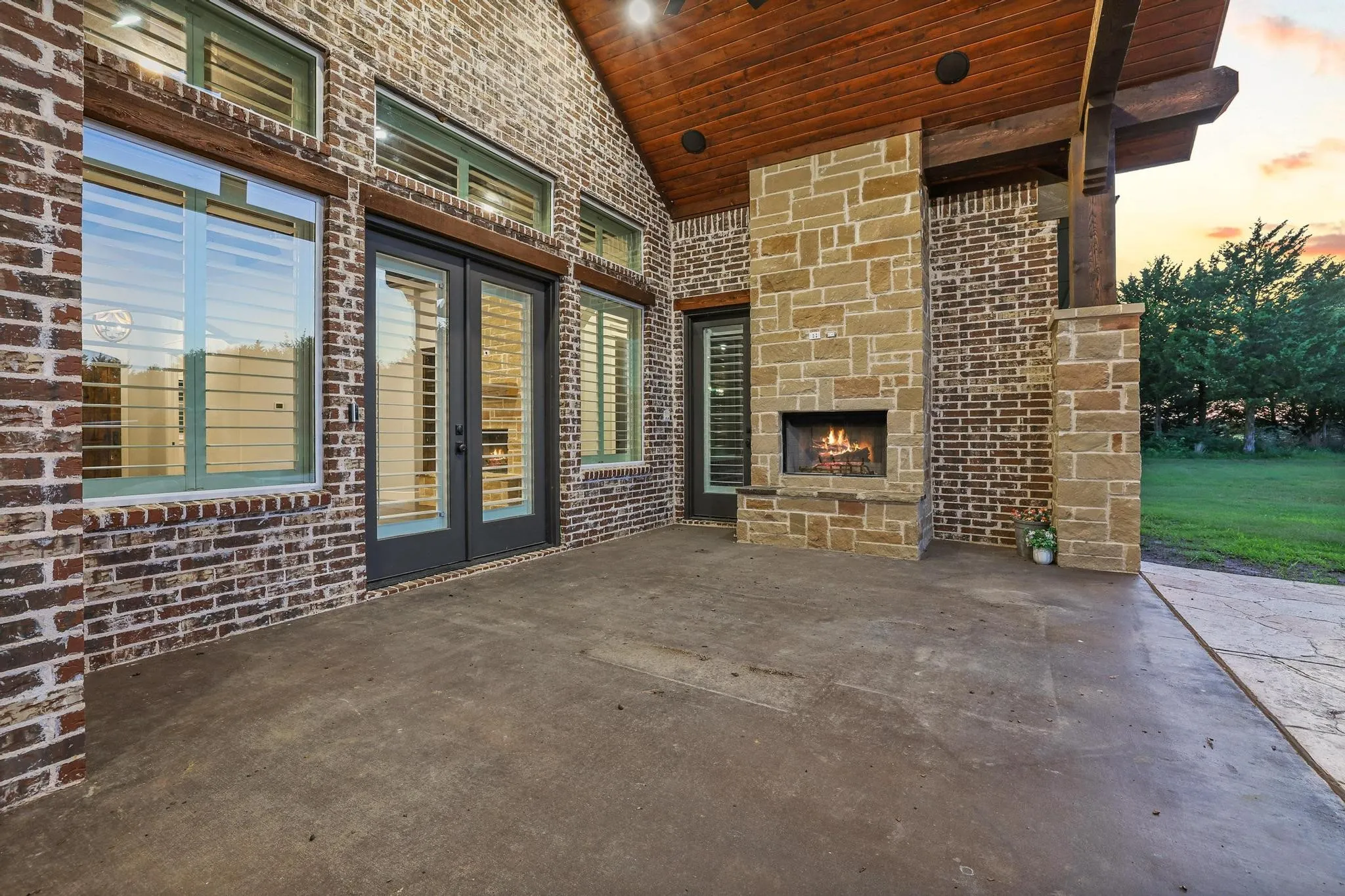 Covered patio featuring an integrated stone fireplace with a raised hearth, dark-stained wood ceiling, and exposed wood beams