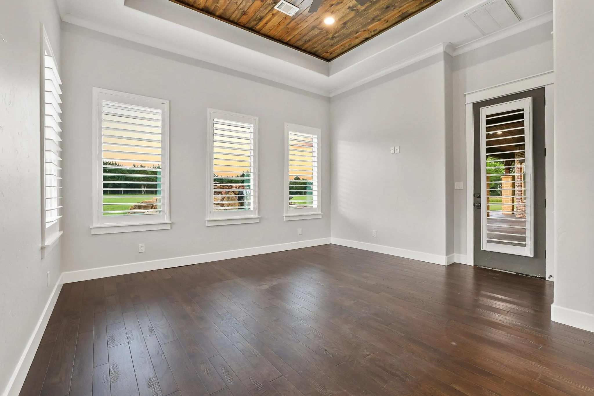 Spacious room featuring dark wood-finish flooring, light-toned walls, and a tray ceiling with a wood-plank accent