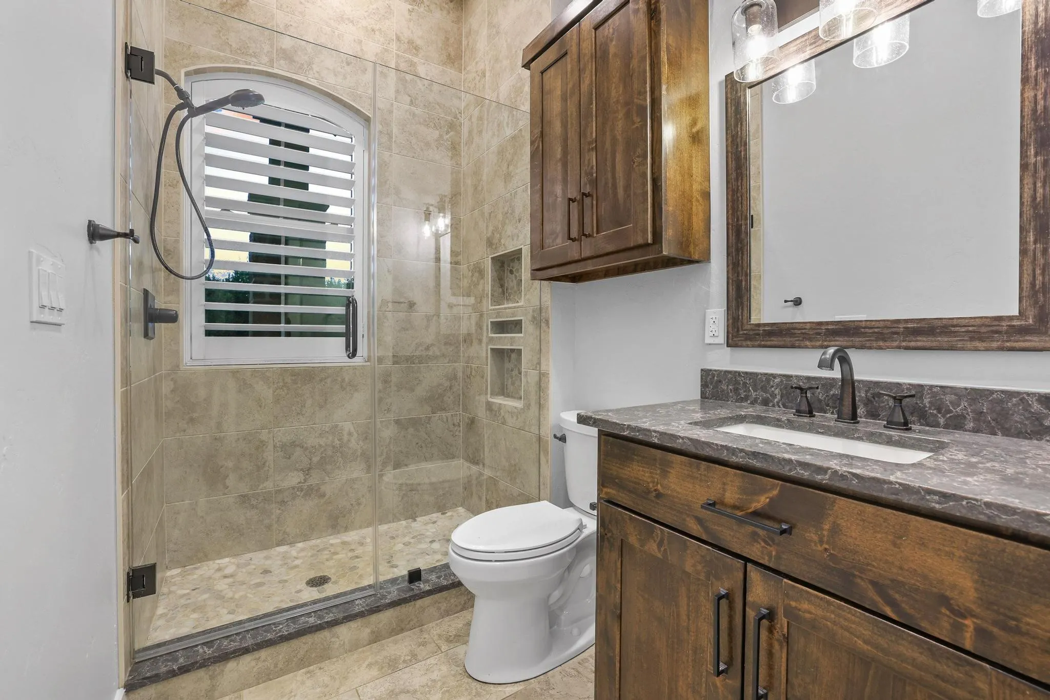 Walk-in shower with clear glass enclosure and pebble-tiled floor