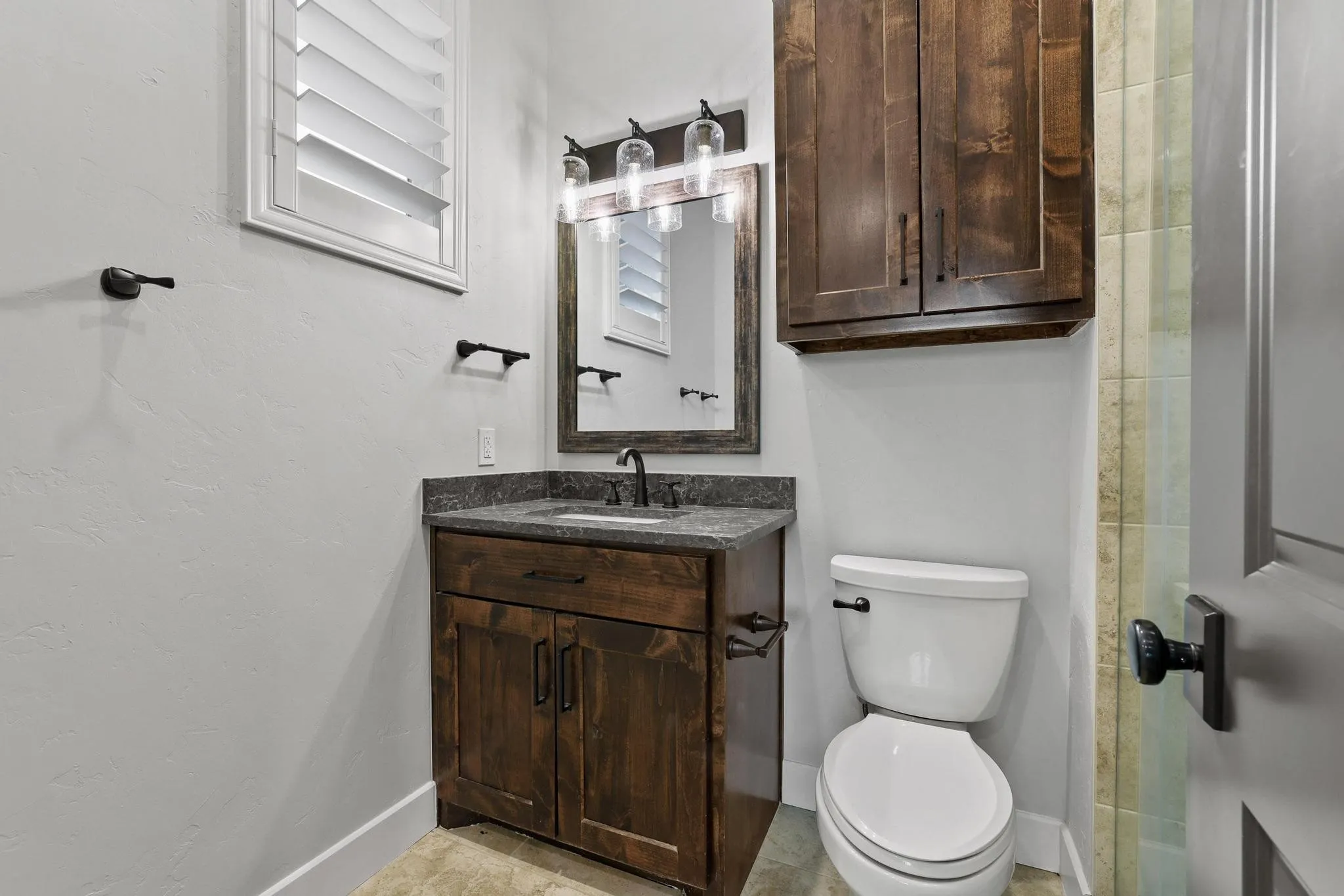 Bathroom vanity with a granite countertop, wood-finish cabinetry, and a dark bronze faucet