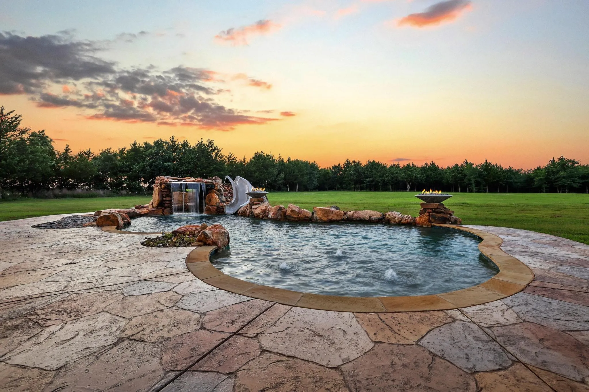 Resort-style pool featuring a rock waterfall, integrated slide, and bubbling water features