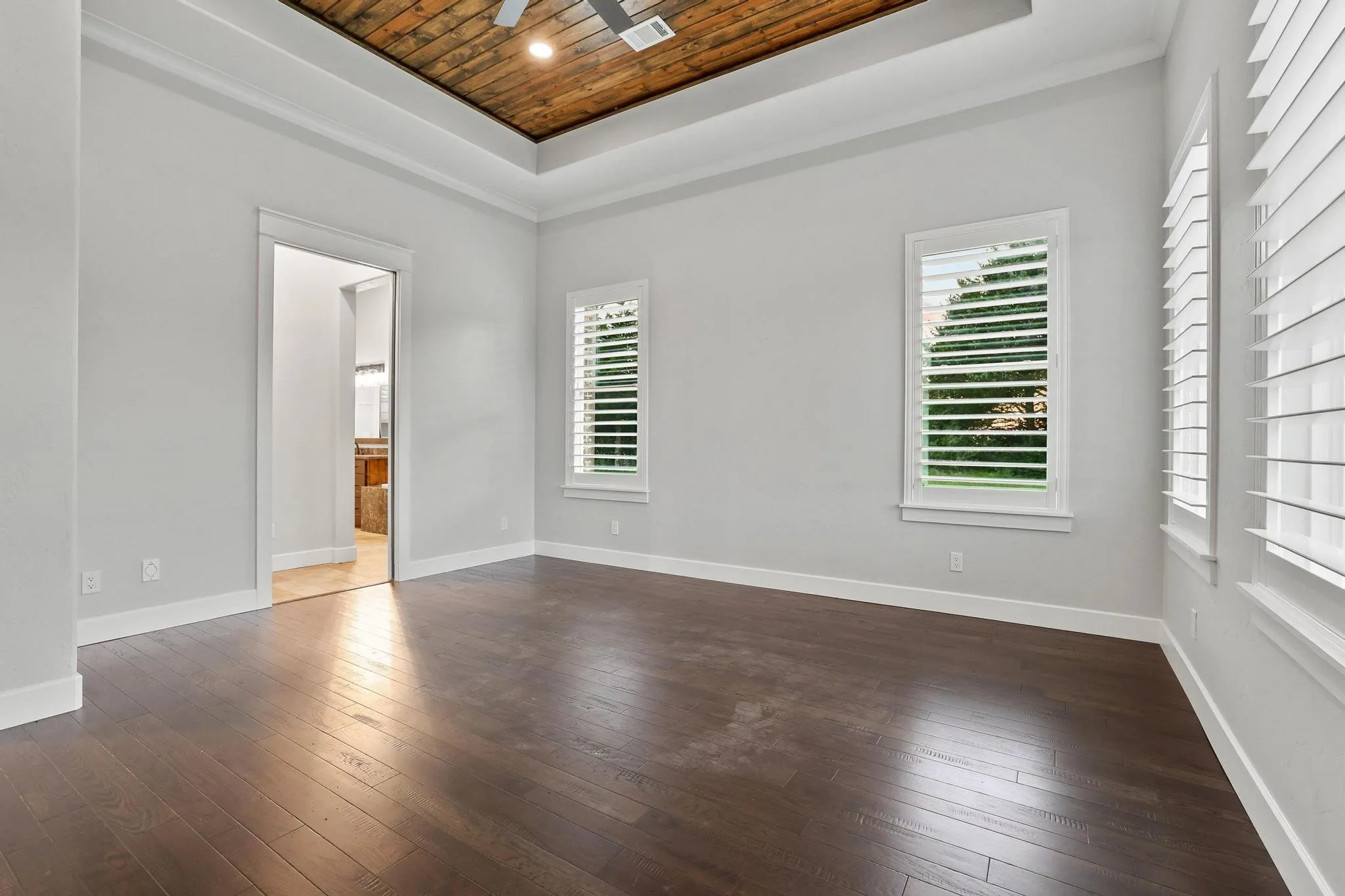 Spacious room featuring rich wood-finish flooring, a tray ceiling with a wood plank inlay, and a ceiling fan