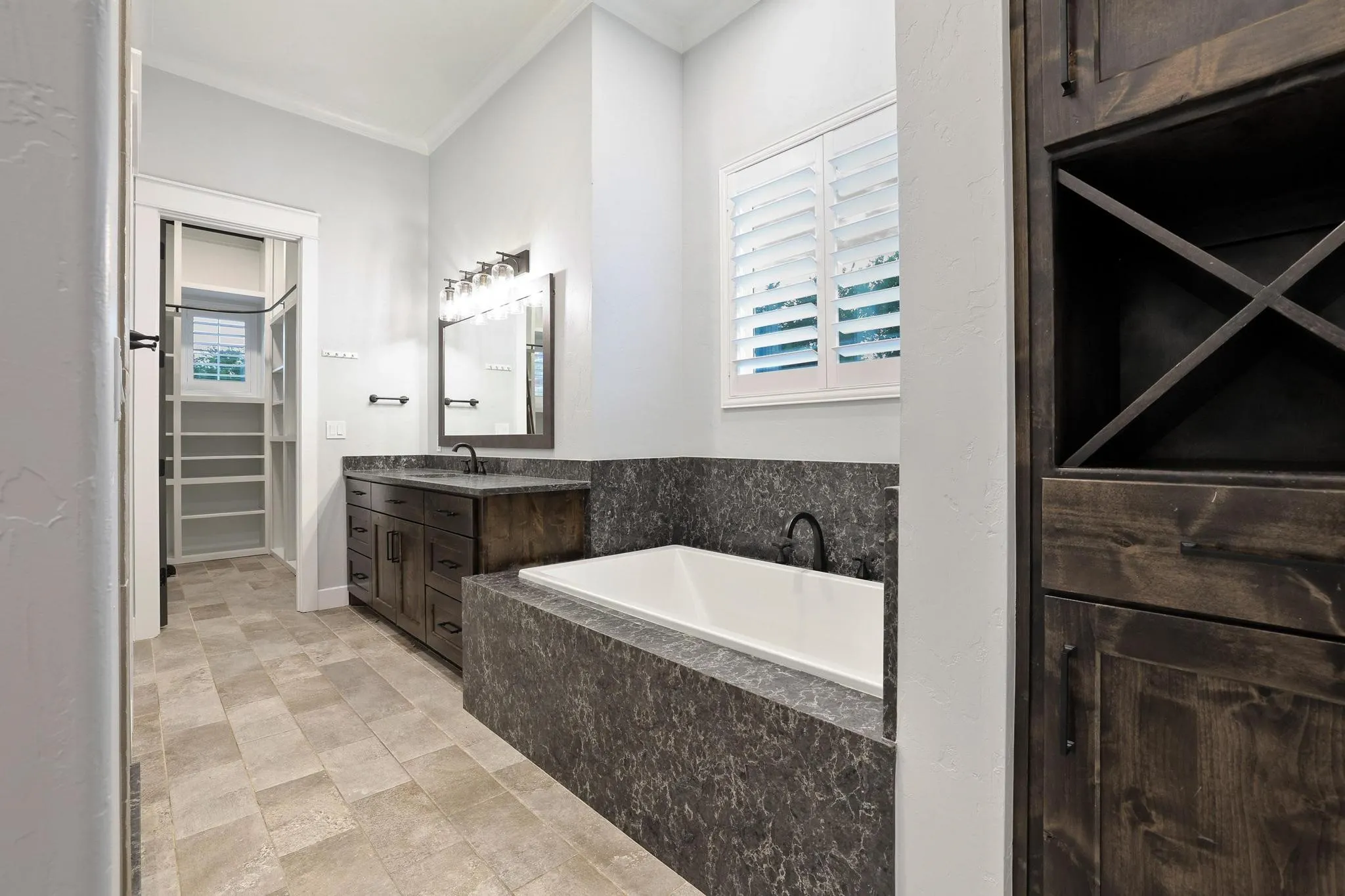 Bathroom featuring a built-in soaking tub with a stone surround, a dark wood-finish vanity with a dark countertop, and tile flooring