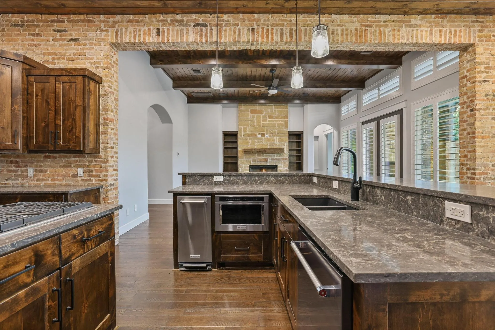 Kitchen featuring dark wood cabinetry, integrated stainless steel appliances, stone countertops, and a black gooseneck faucet