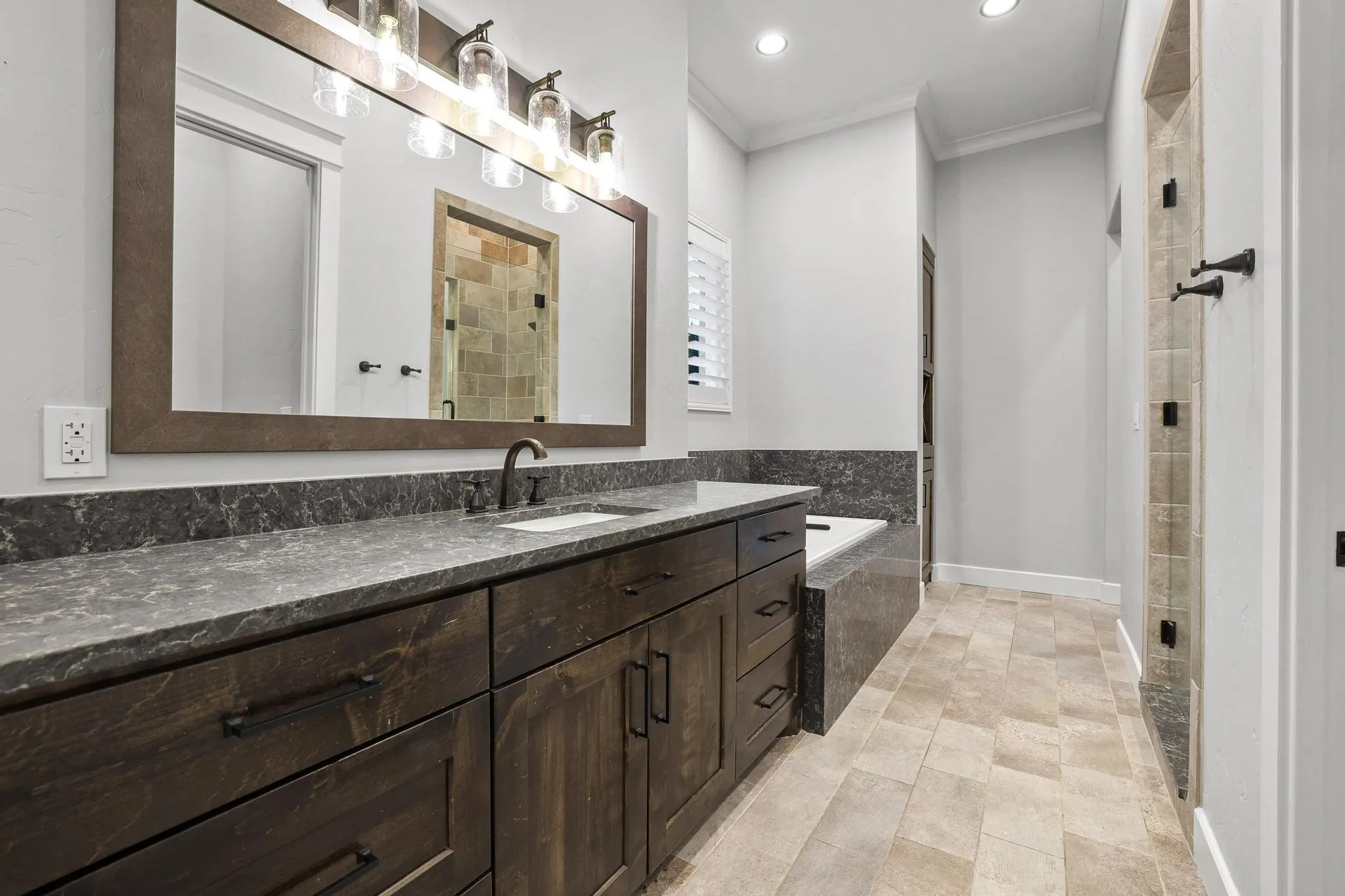 Spacious bathroom featuring a dark wood-finish vanity with a single sink, dark stone countertop, and an expansive framed mirror