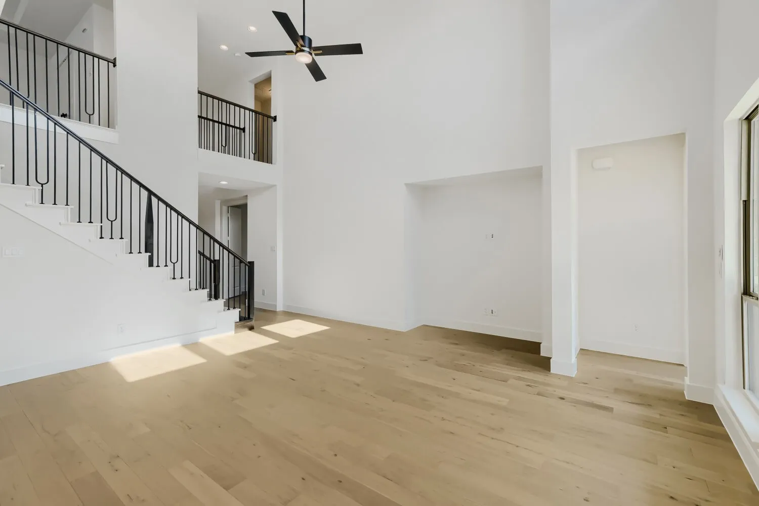 Two-story ceiling height, light wood-finish flooring, staircase with wrought iron balusters, recessed lighting, and a ceiling fan