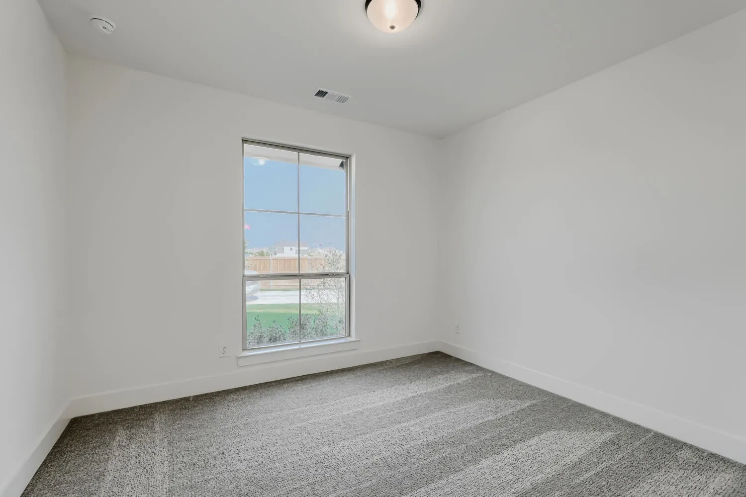 White walls, gray patterned carpet, and a flush-mount ceiling light
