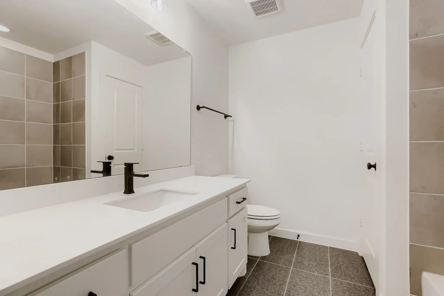 Modern primary bathroom featuring a double-sink vanity with white cabinetry, quartz countertop, and matte black hardware