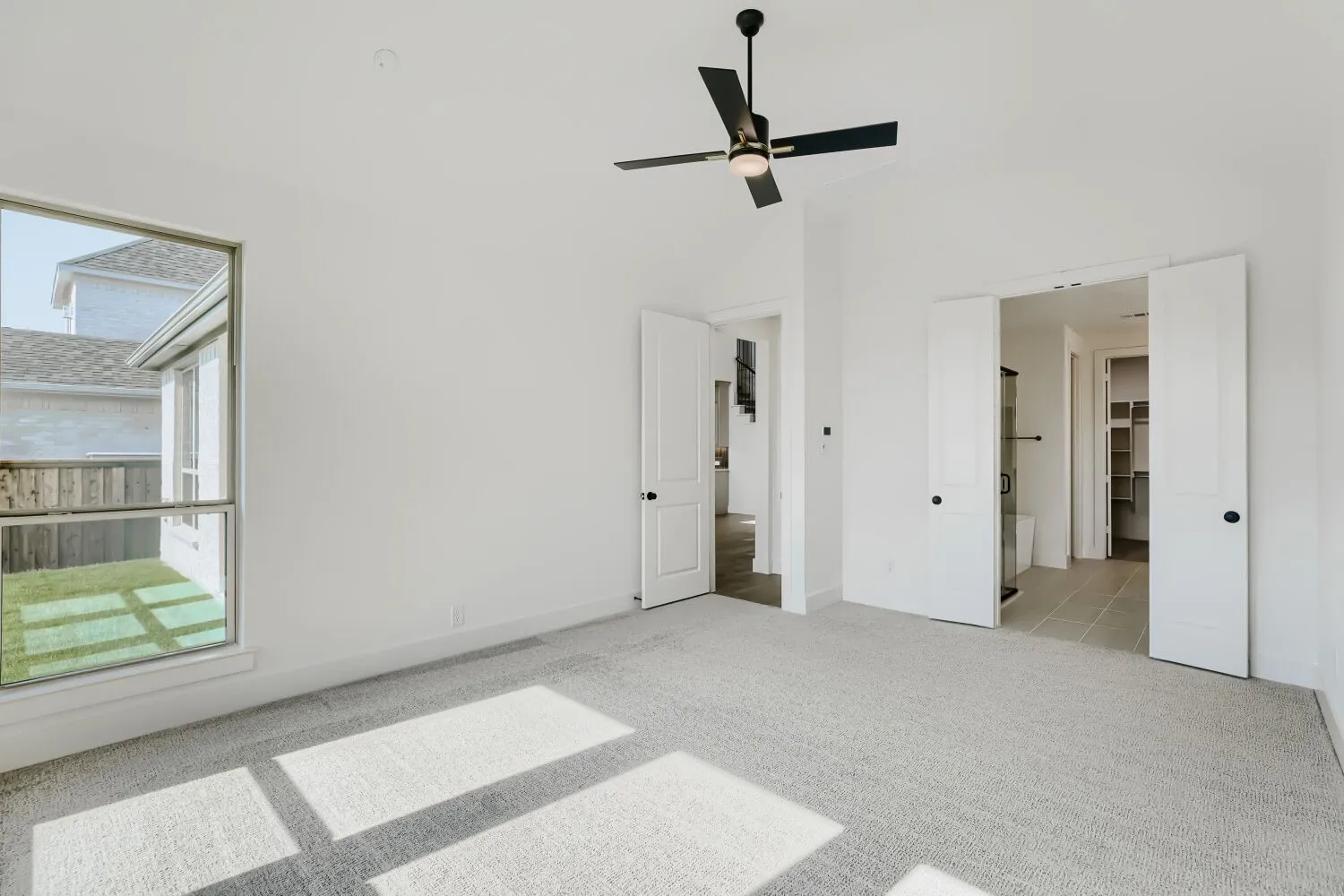 Spacious room featuring light-toned carpeting, a large window, and a ceiling fan
