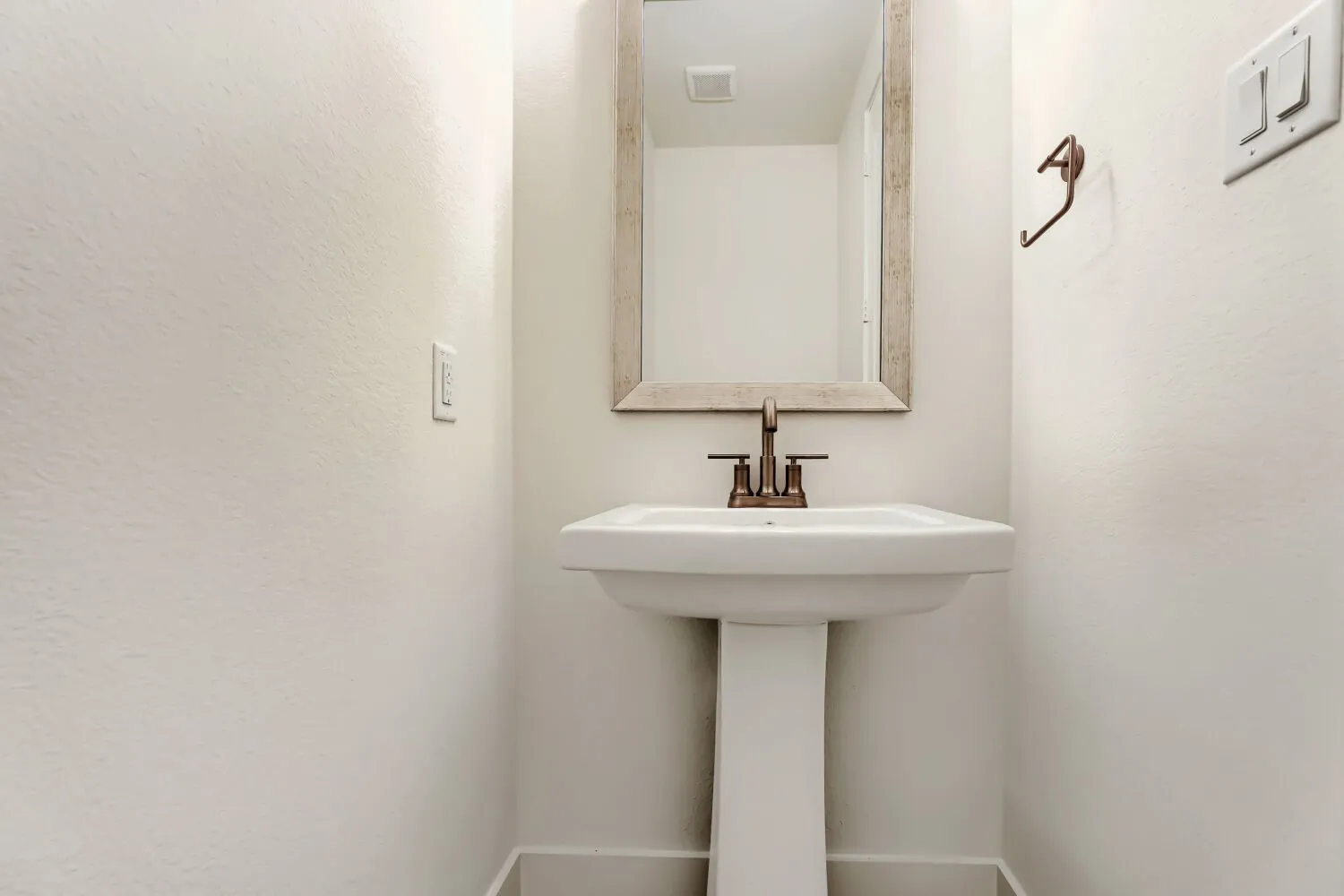 Pedestal sink with bronze-finish faucet, framed mirror, and light-toned walls