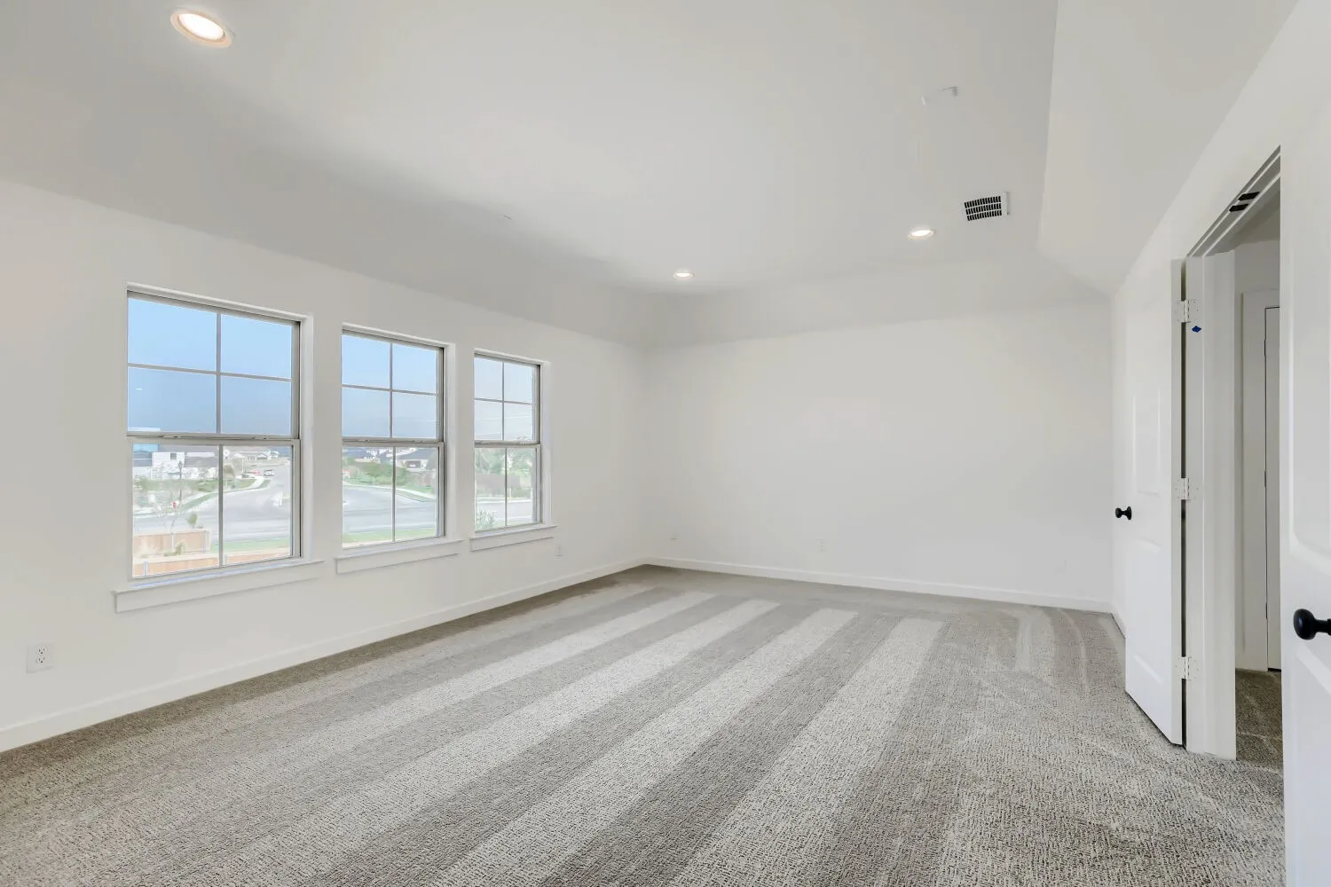 Recessed lighting, three large windows, white trim, and light-toned patterned carpet