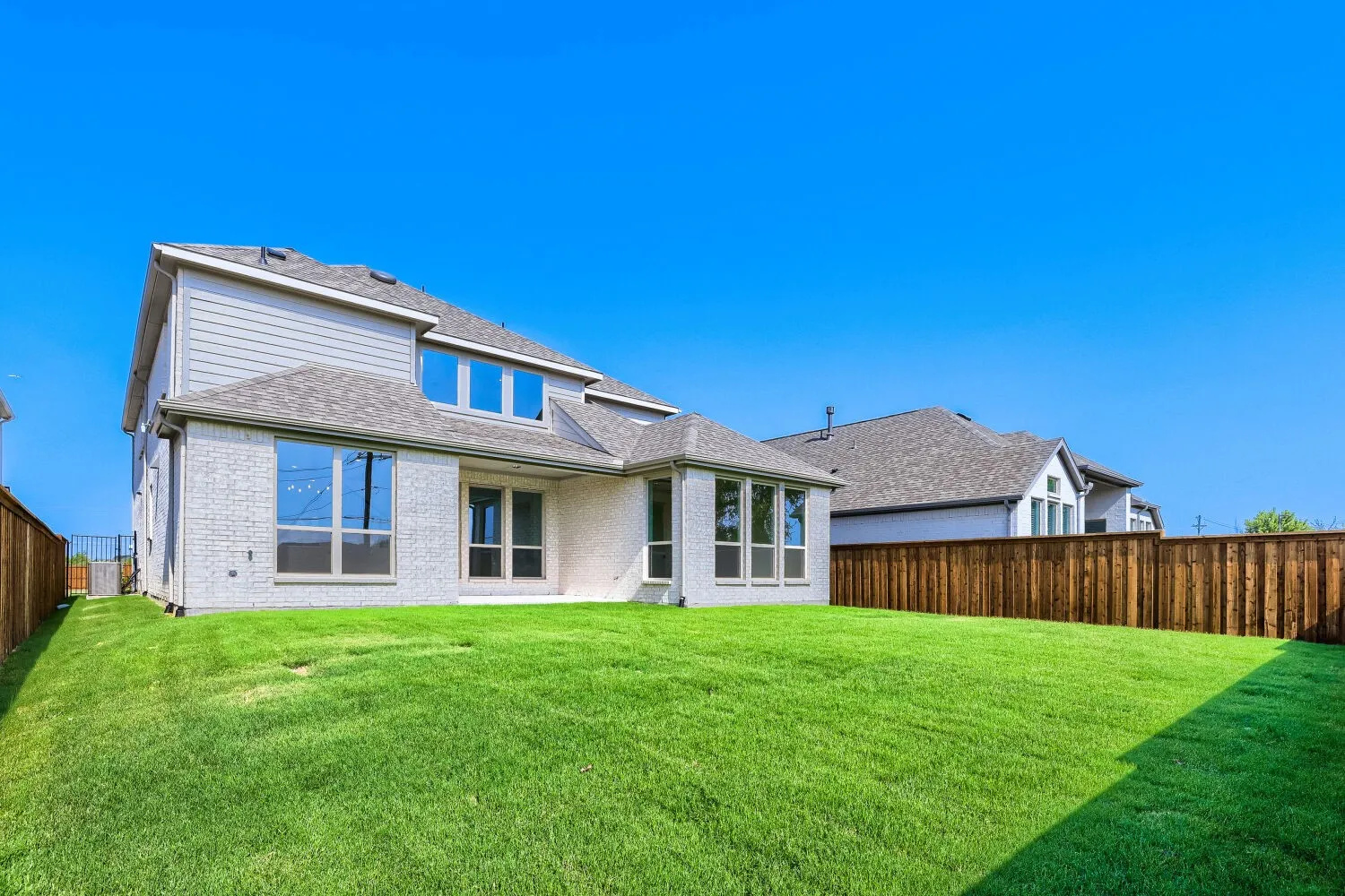 Expansive backyard featuring a manicured lawn, full privacy fencing, and a white brick exterior