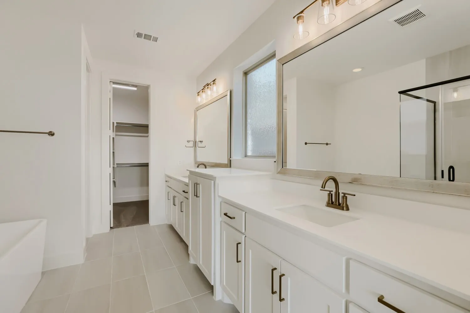 Dual vanity with white cabinetry and integrated sinks, a walk-in shower with clear glass enclosure, a freestanding soaking tub, and a walk-in closet with shelving