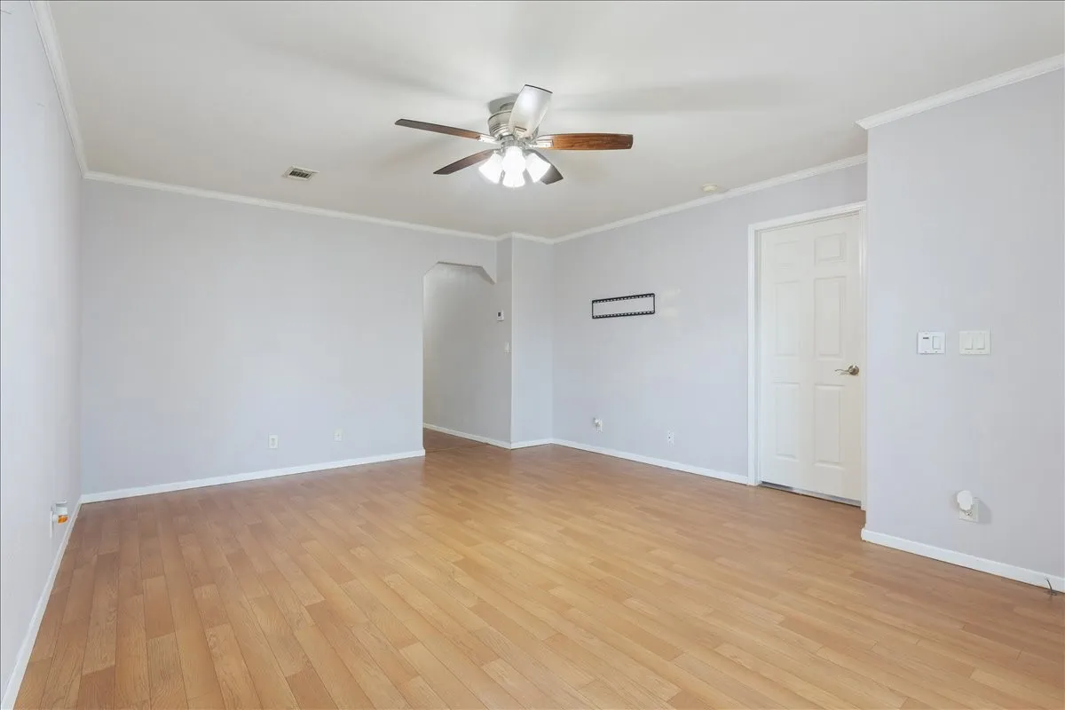 Spacious room featuring wood-finish flooring, light gray walls, white trim, a ceiling fan with light fixture, and an arched doorway