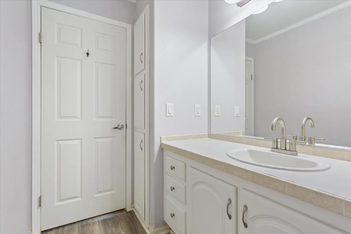 Vanity area featuring a built-in sink with a brushed nickel faucet, large wall-mounted mirror, white paneled cabinetry with curved hardware, and durable wood-finish flooring