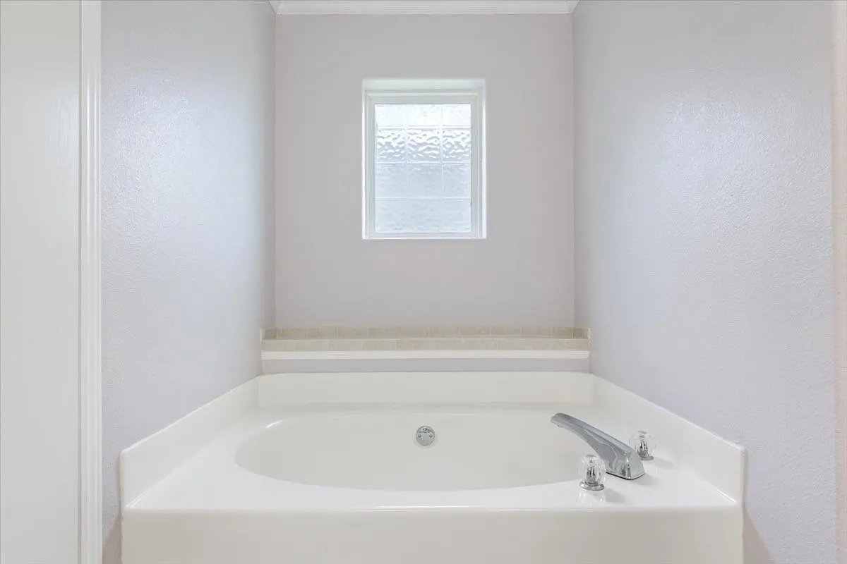Corner built-in tub with deck-mounted chrome fixtures, white acrylic basin, and a tiled surround