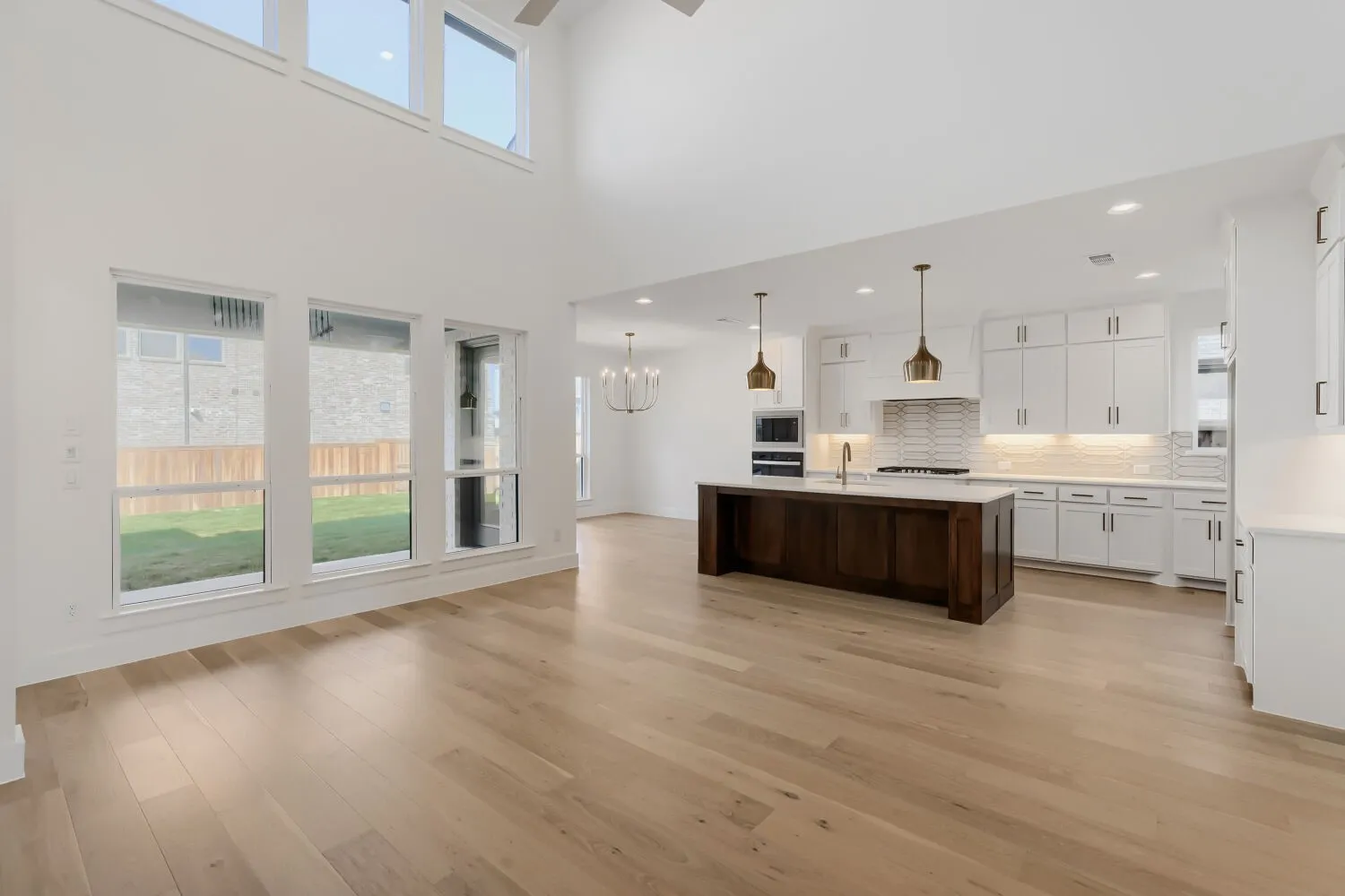 Open-concept living area featuring high ceilings, wood-finish flooring, a large kitchen island with pendant lighting, and white cabinetry