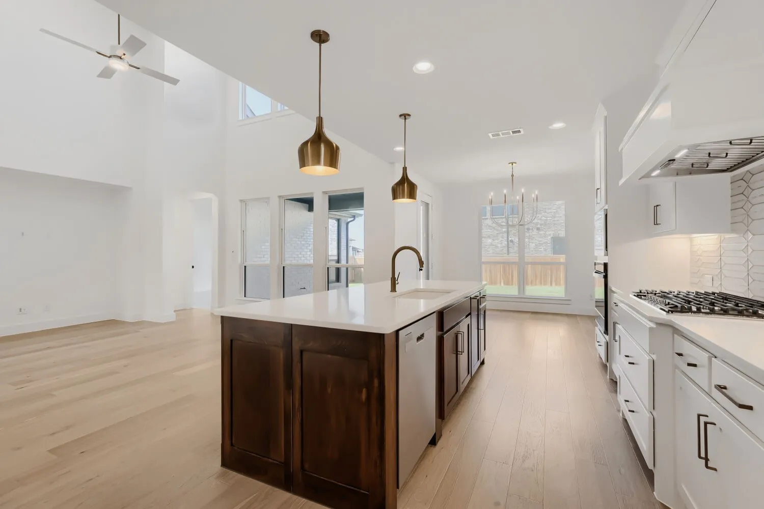 Kitchen island with integrated sink, stainless steel appliances, white cabinetry, and light wood-finish flooring