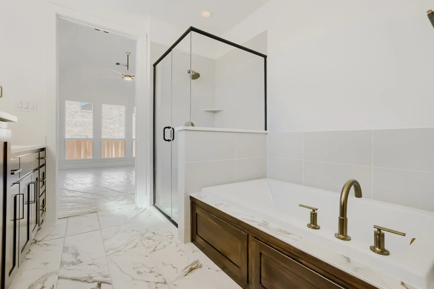Enclosed shower with black frame, built-in bathtub with brass fixtures, wood-finish paneling, and marble-look tile flooring