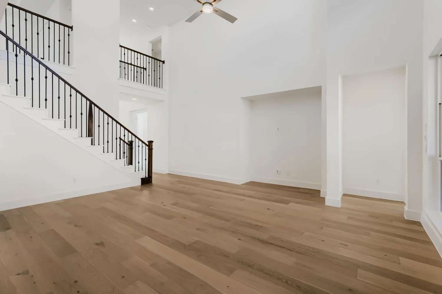 Soaring ceilings with integrated lighting, wood-finish flooring, two-story staircase with decorative iron balusters, and built-in wall niches