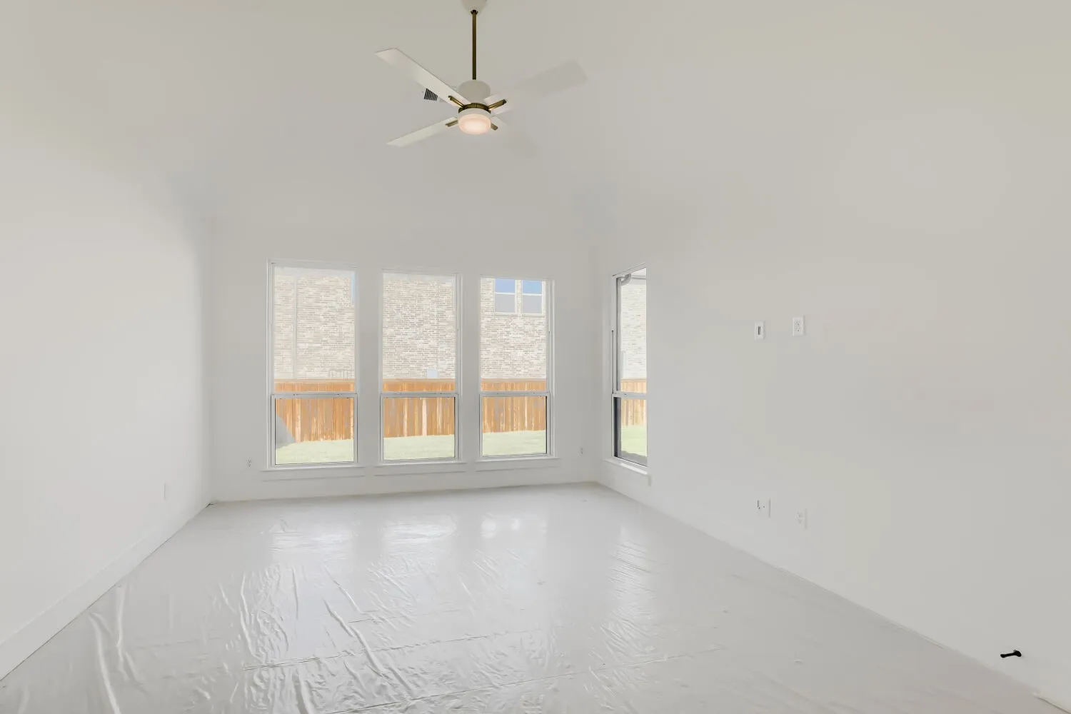 Vaulted ceiling with a flush-mount ceiling fan, multiple windows with roller shades, and white walls