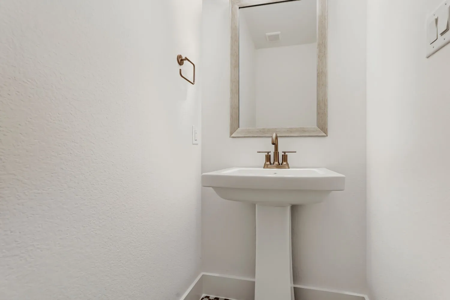 Pedestal sink with a bronze-finish faucet, framed mirror, and coordinating bronze-finish towel ring