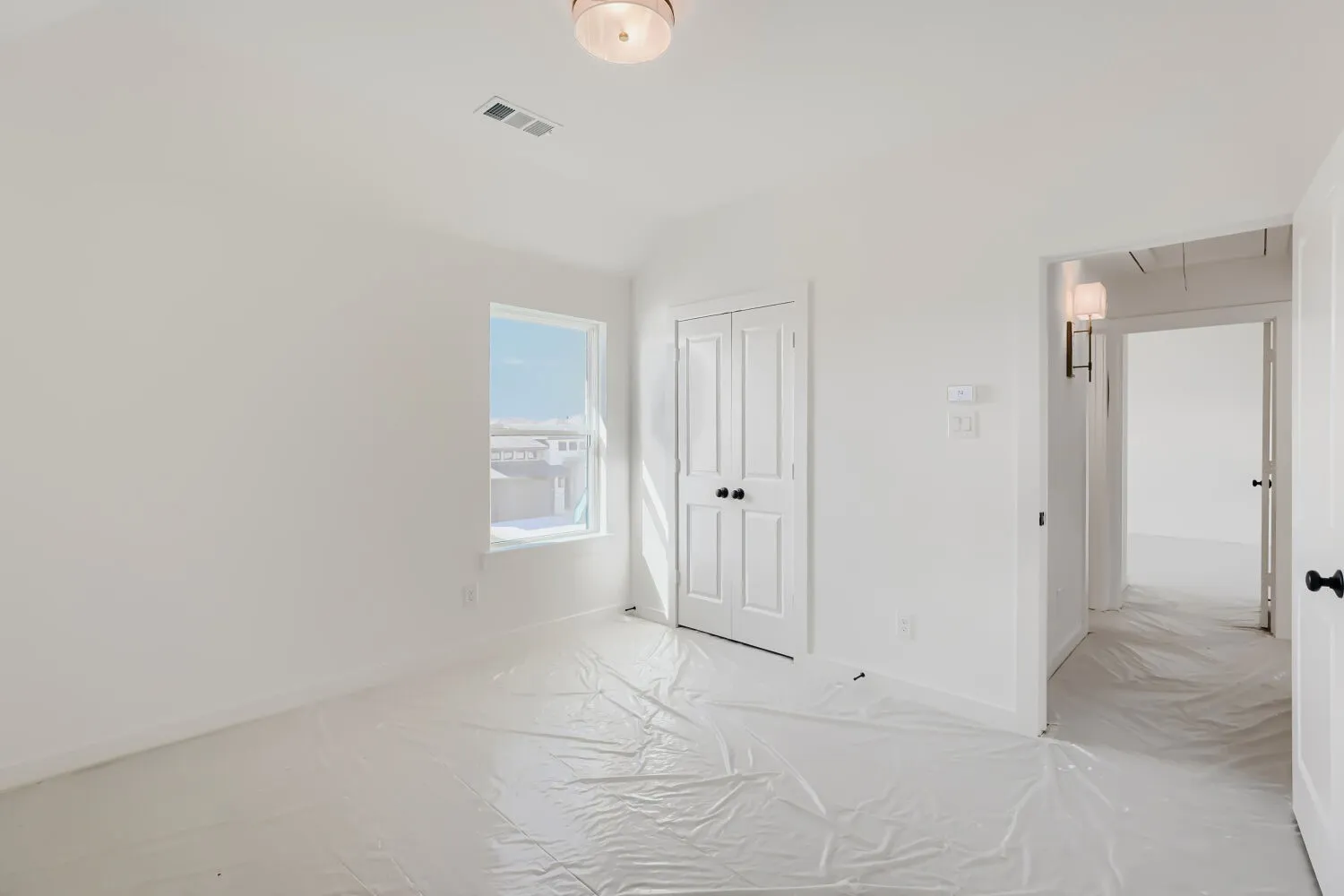 White walls and trim, window with natural illumination, white bi-fold closet doors with black hardware, and an overhead light fixture