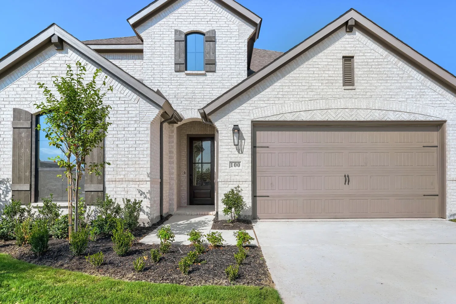 White brick exterior with dark wood shutters, arched entry, and an integrated two-car garage