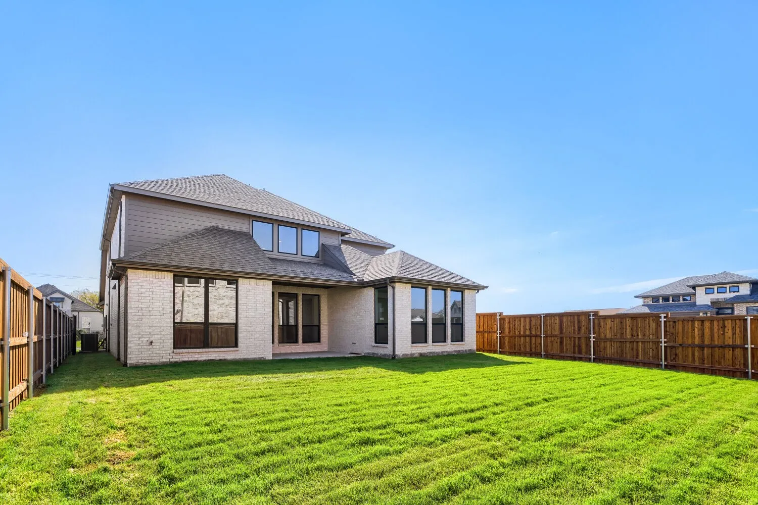 Expansive backyard featuring a green lawn, wood fencing, and a two-story exterior with light-toned brick and siding