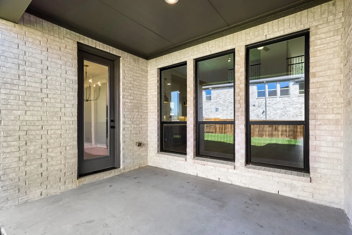 Covered patio featuring a concrete surface, white brick exterior, black-framed windows, and a black-framed glass-paneled door