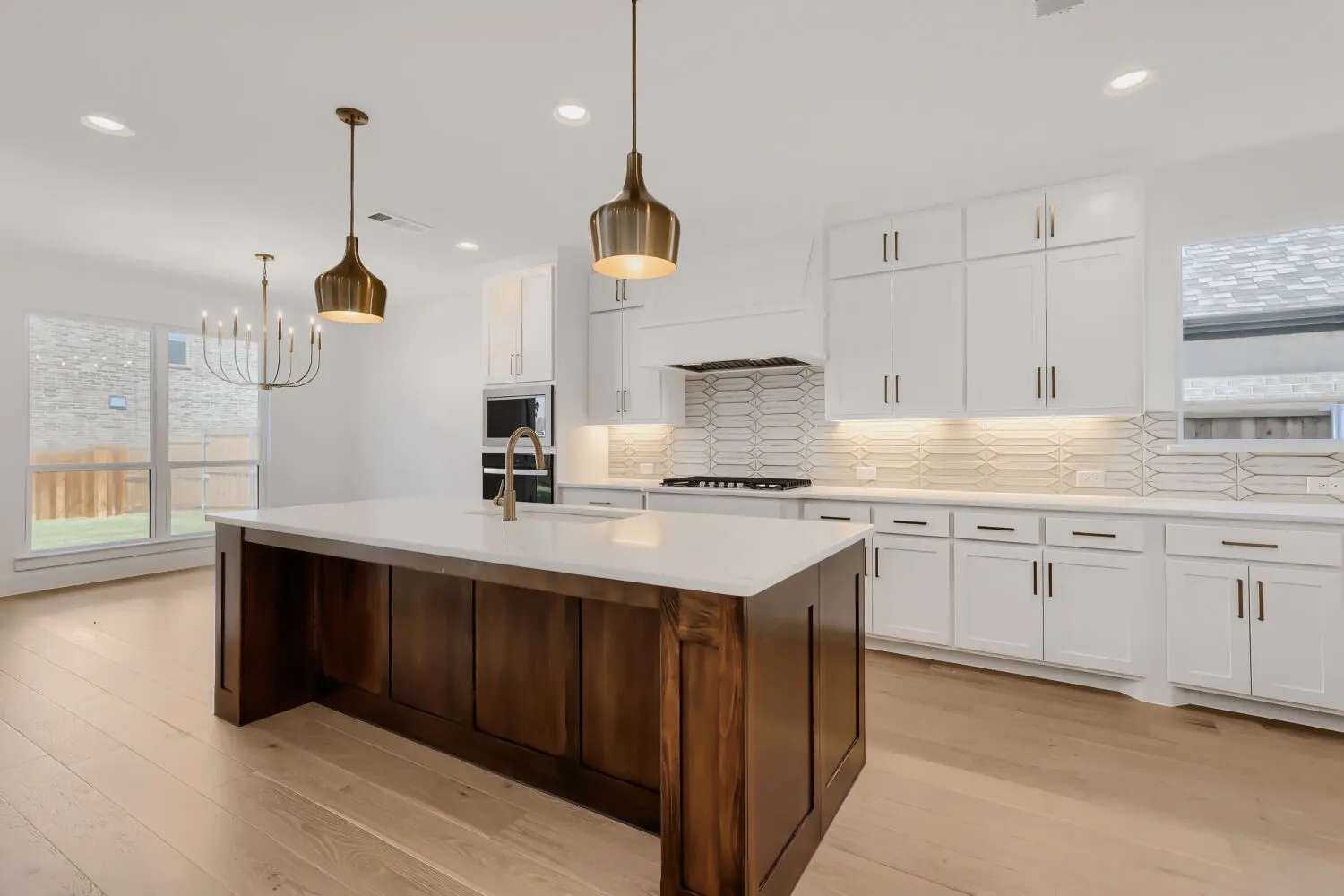 Spacious kitchen featuring an expansive center island, light wood-finish flooring, white cabinetry, integrated stainless steel appliances, and a unique tiled backsplash