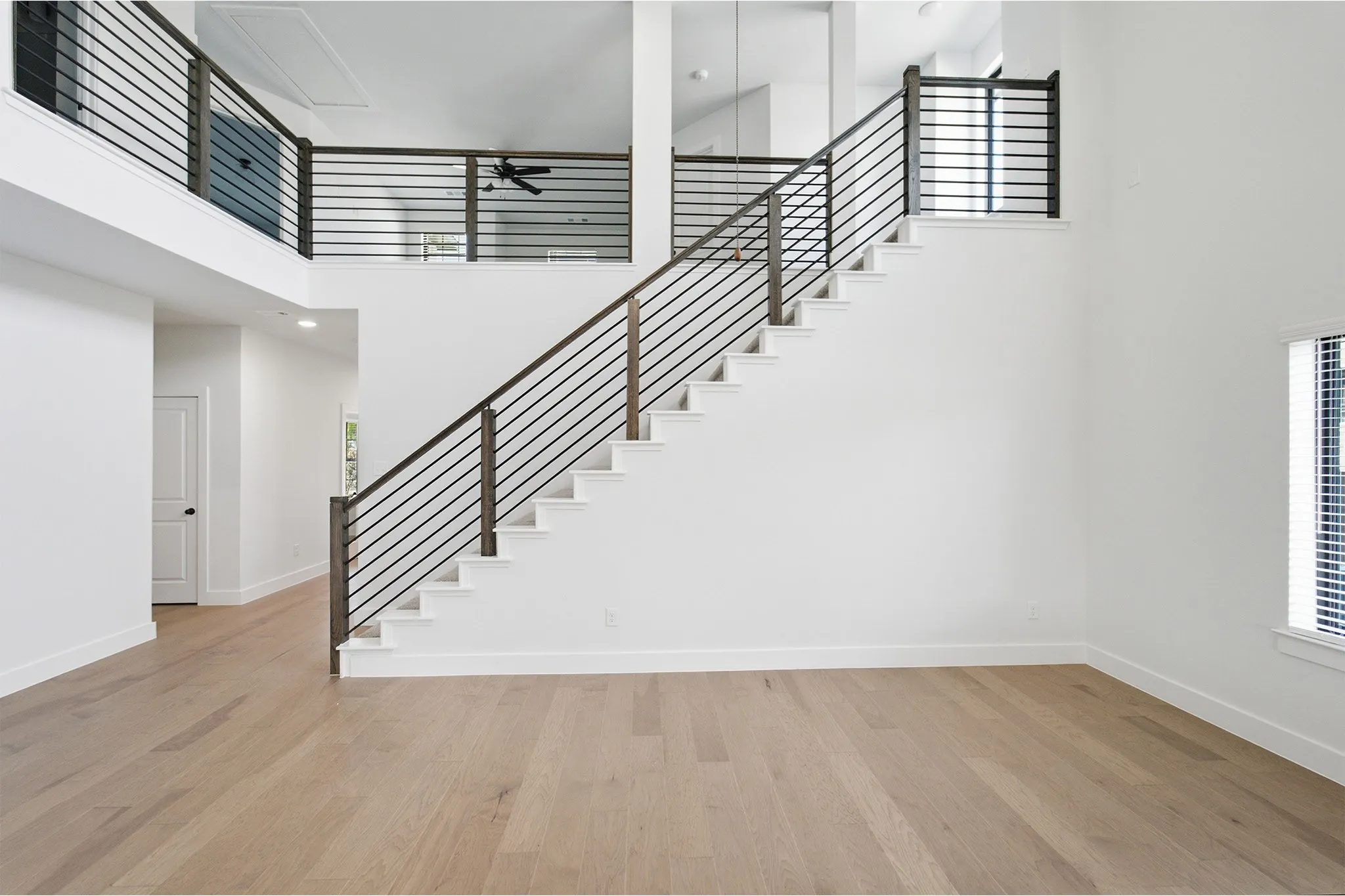 Double-height entryway with a contemporary staircase featuring horizontal metal balusters and wood newel posts