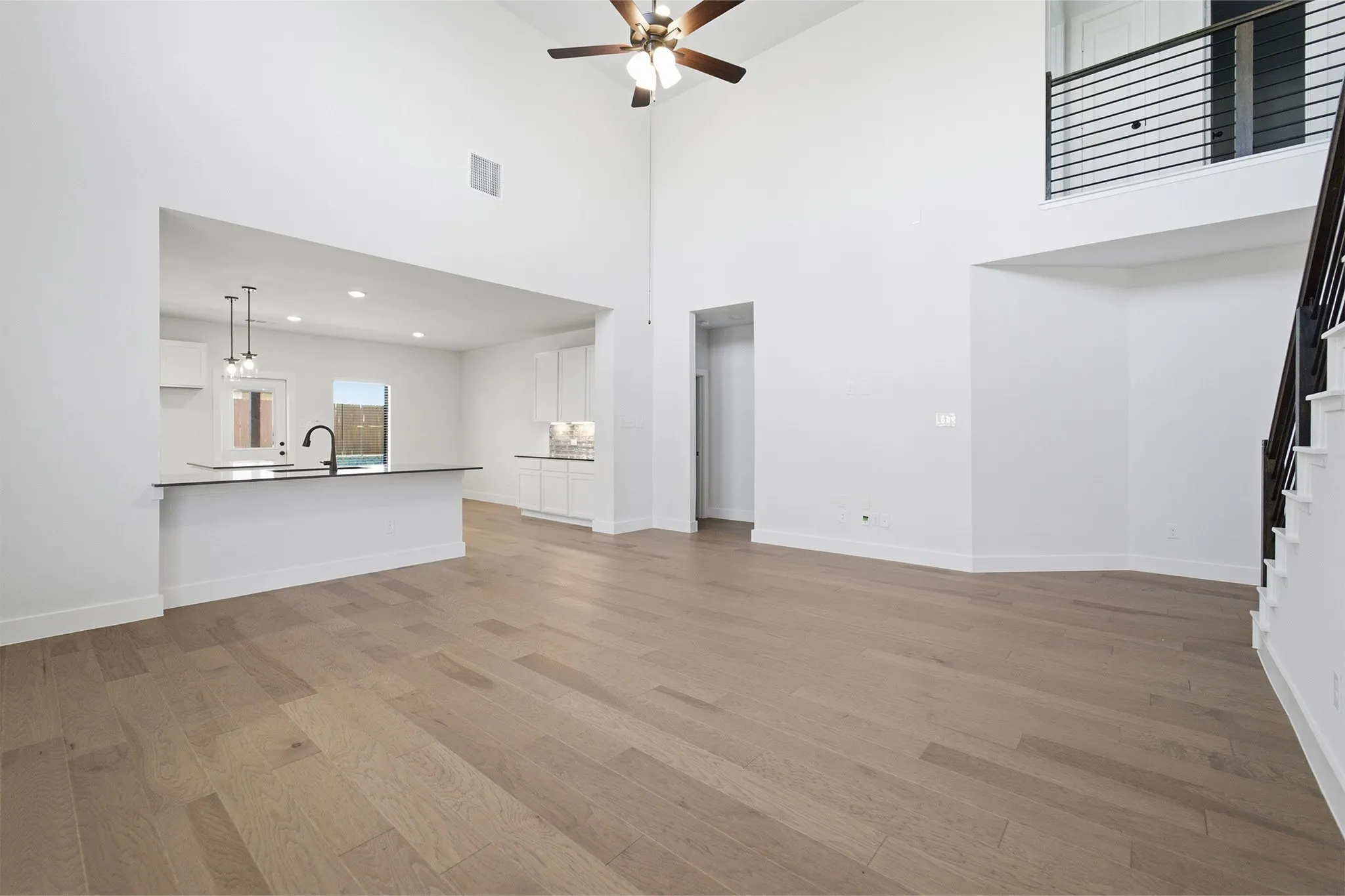 Spacious living area featuring high ceilings, wood-finish flooring, and a contemporary ceiling fan