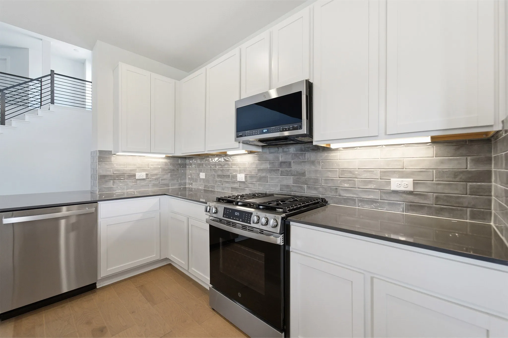 Modern kitchen featuring white cabinetry, dark countertops, a subway tile backsplash, stainless steel appliances, and wood-finish flooring