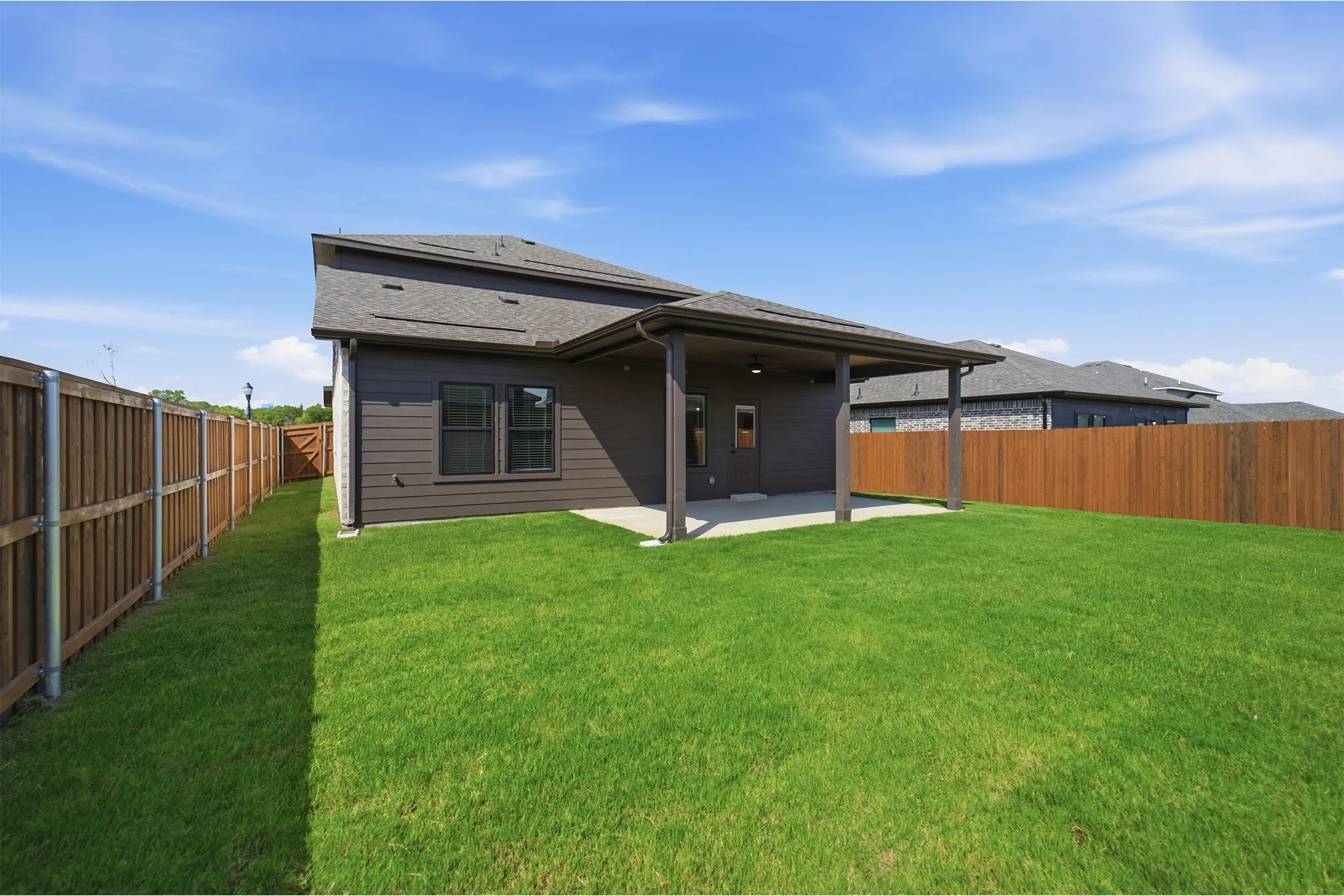 Expansive grassy yard featuring a covered patio, full privacy fencing, dark siding, and a dark shingle roof