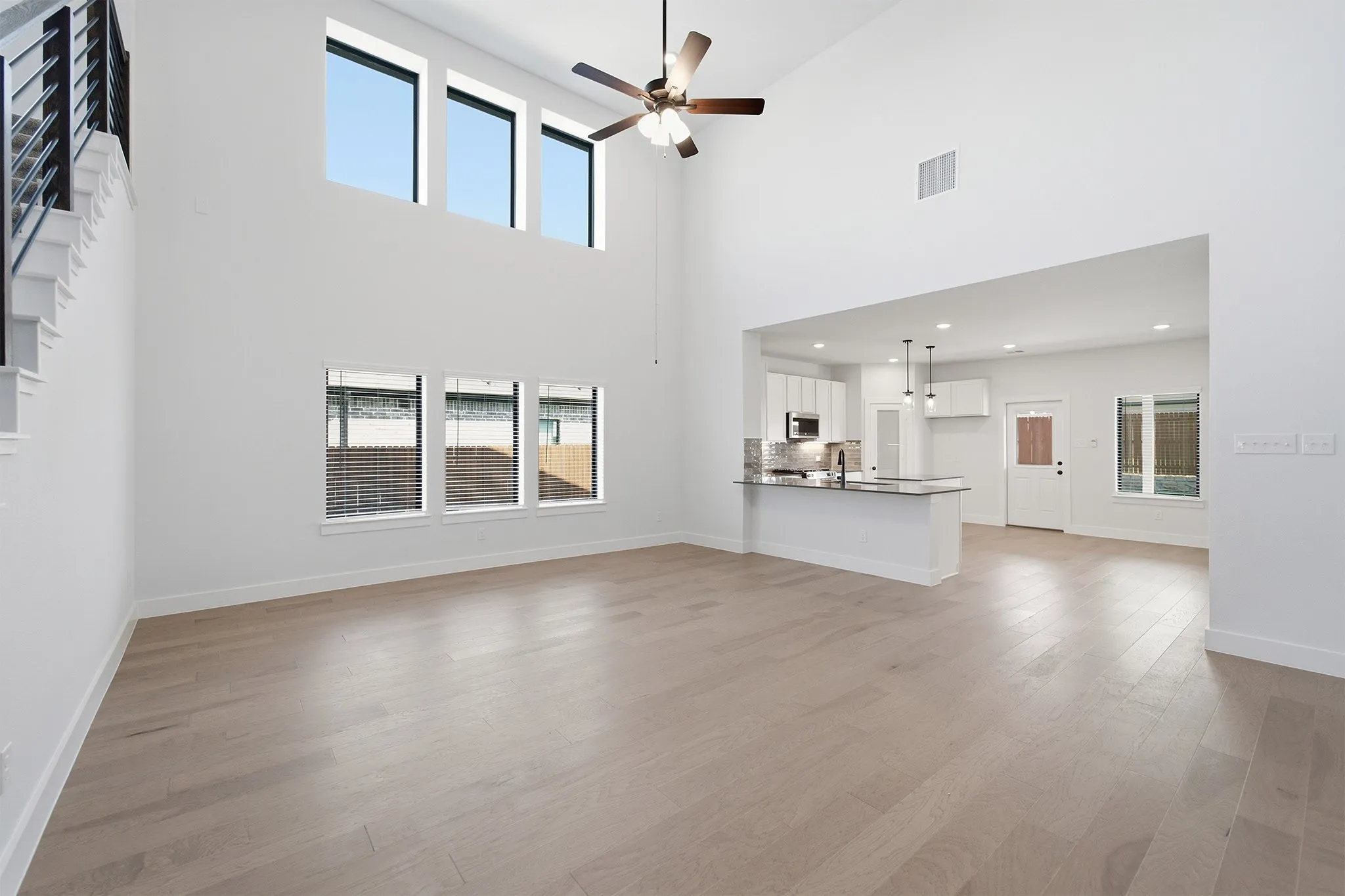 Open-concept living area featuring a vaulted ceiling with a ceiling fan, light wood-finish flooring, and multiple windows