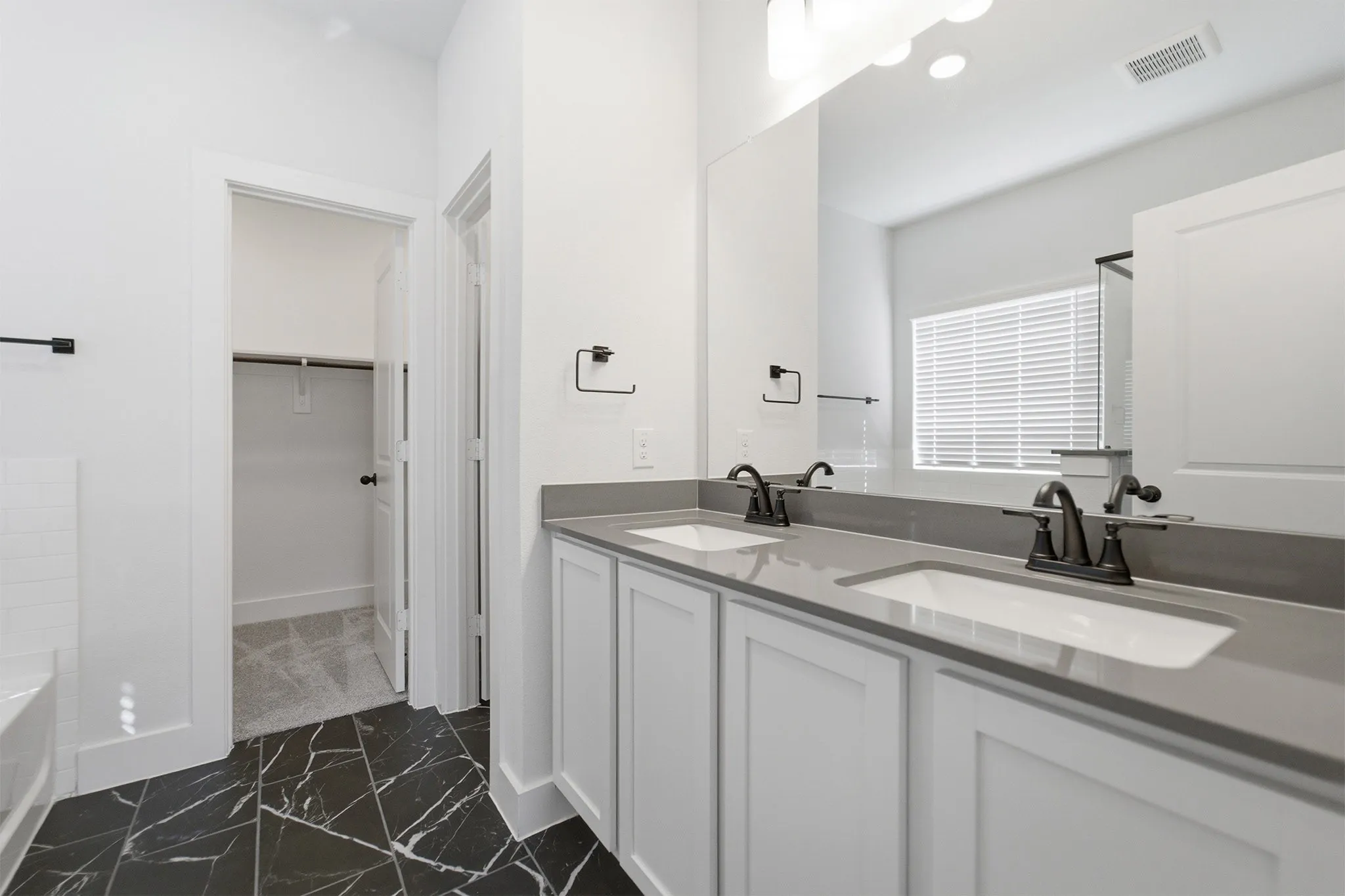 Dual vanity featuring white shaker cabinetry, undermount sinks, and grey countertops with matte black fixtures