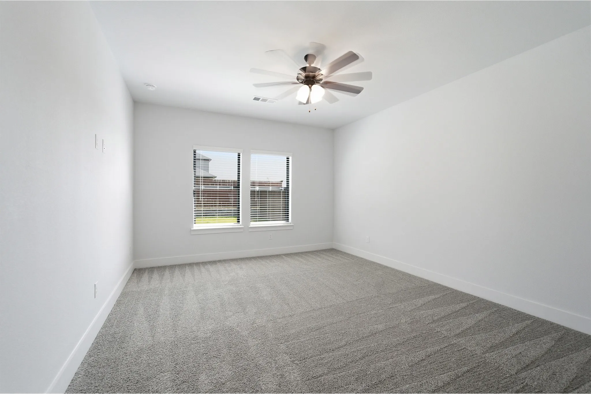 Spacious interior room featuring a vaulted ceiling with a flush-mount ceiling fan and integrated lighting, two windows with horizontal blinds, neutral-toned patterned carpet, and clean white walls with matching baseboards