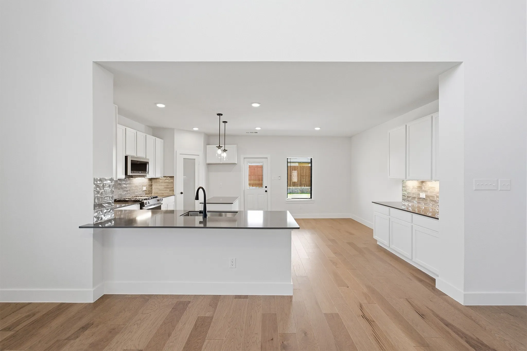 Open-concept kitchen featuring an island with an undermount sink and matte black faucet, white cabinetry, dark countertops, and wood-finish flooring