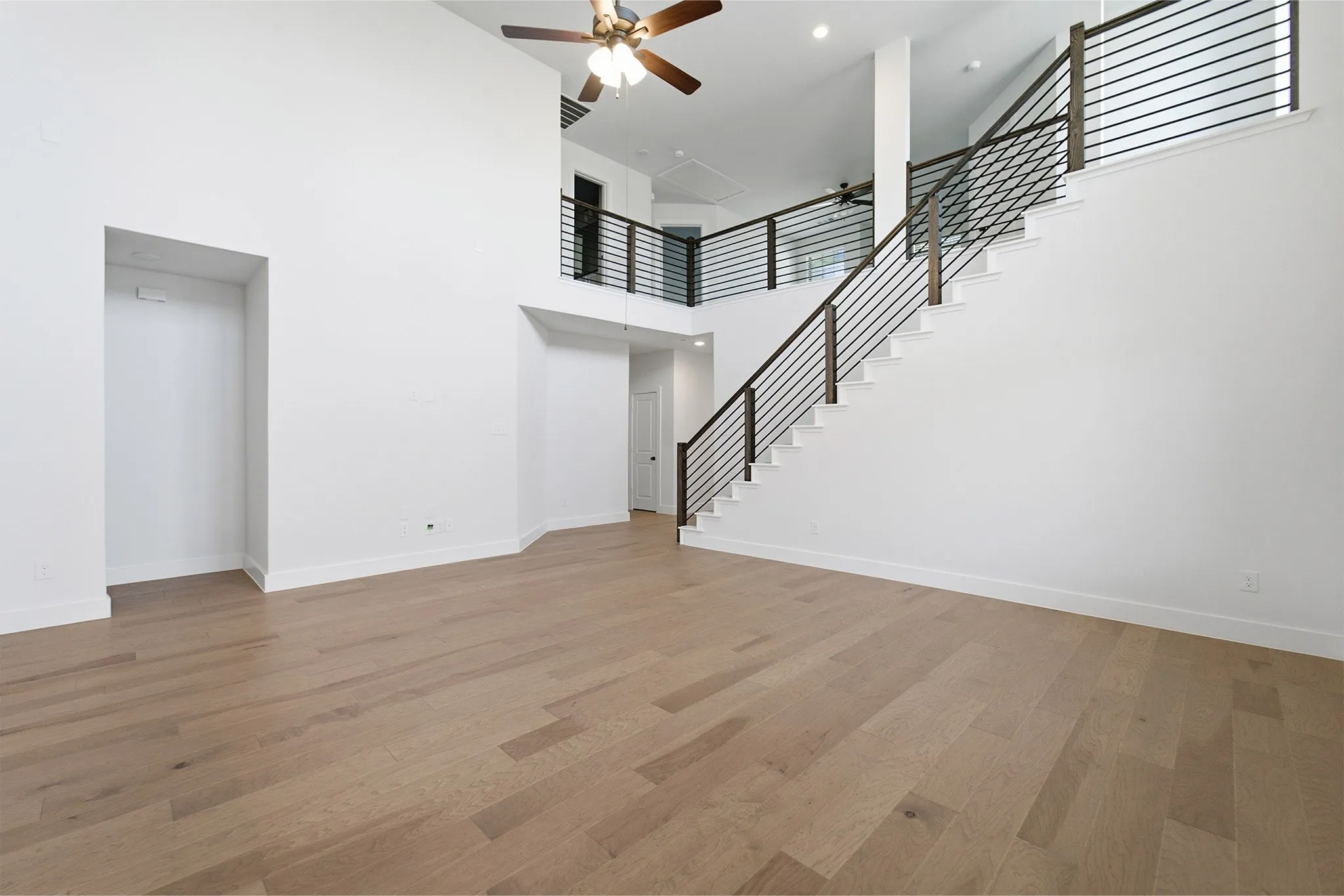 Two-story interior featuring light wood-finish flooring and a modern open-tread staircase with horizontal iron railings