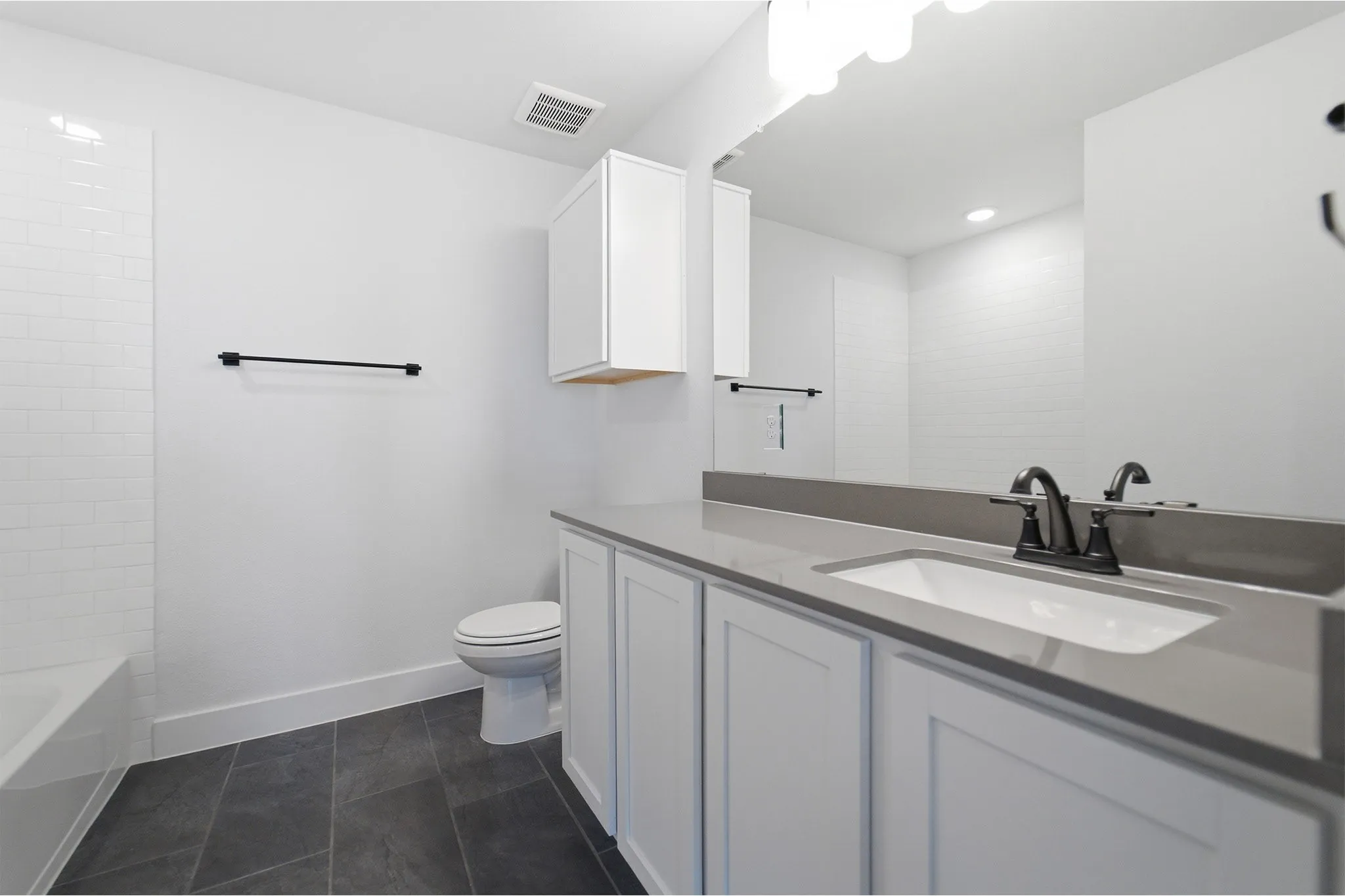 Contemporary bathroom featuring a white vanity with paneled doors, a rectangular undermount sink, a gray countertop, and dark-finish fixtures