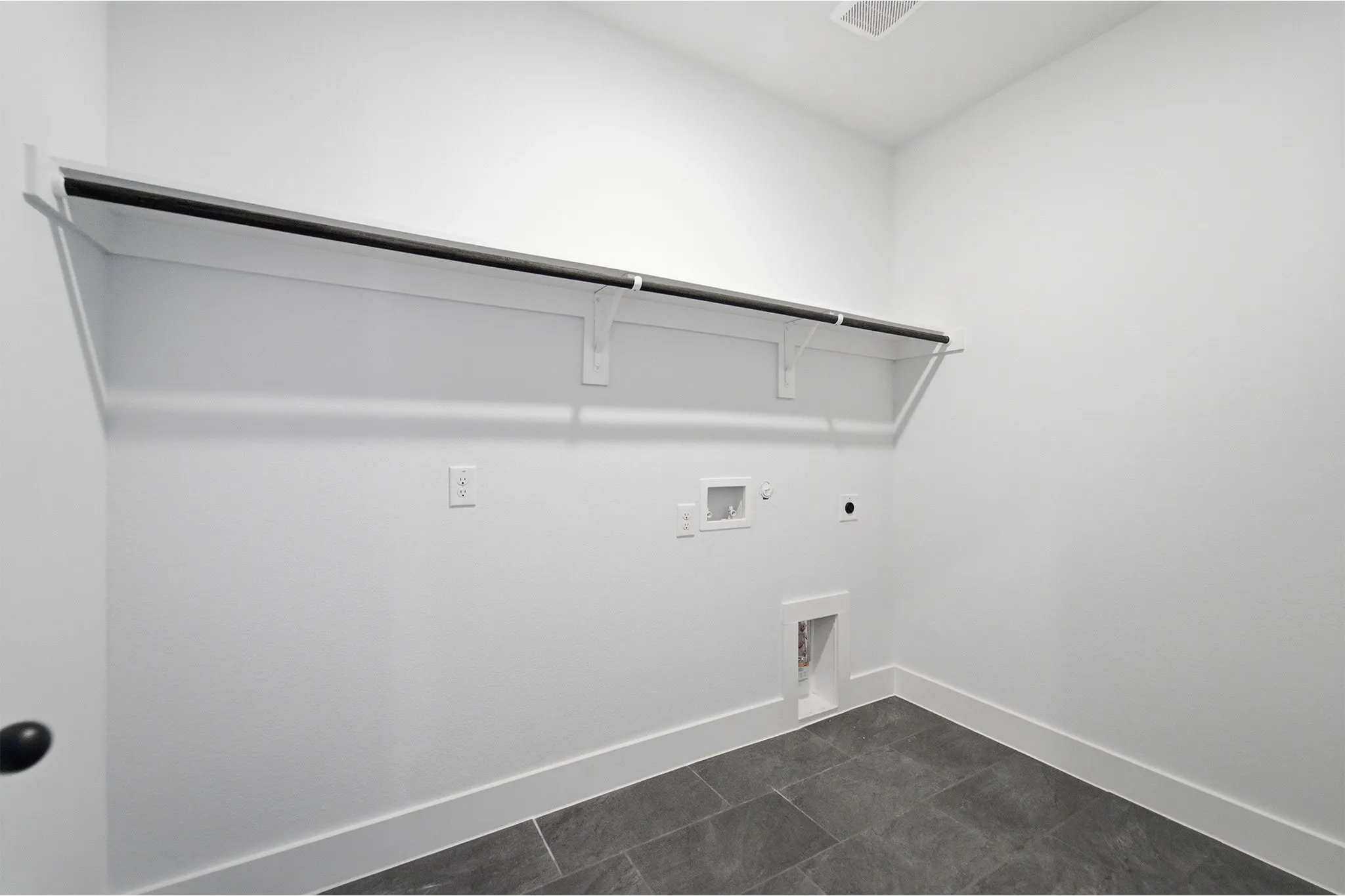 Dedicated utility space featuring a built-in shelving unit with hanging rod, appliance hookups, dark rectangular floor tiles, and white baseboards