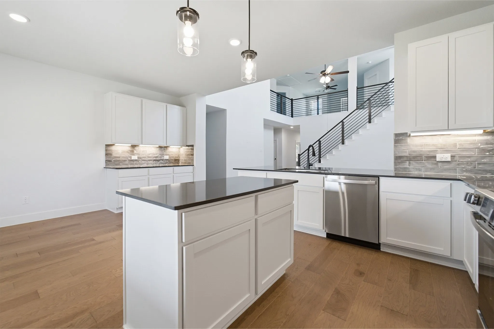 Modern kitchen featuring white shaker cabinetry, dark countertops, a stainless steel dishwasher, and wood-finish flooring