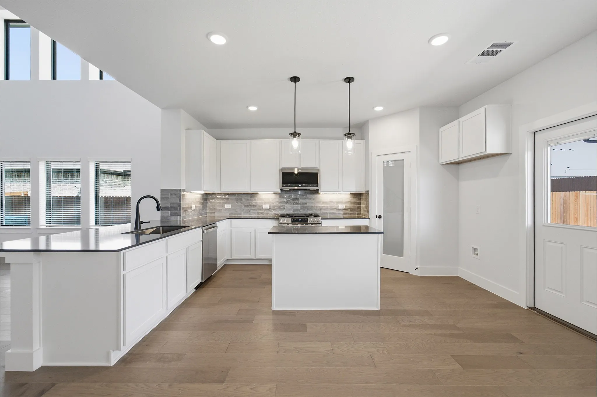 Modern kitchen featuring white cabinetry, dark countertops, stainless steel appliances, and a gray tile backsplash