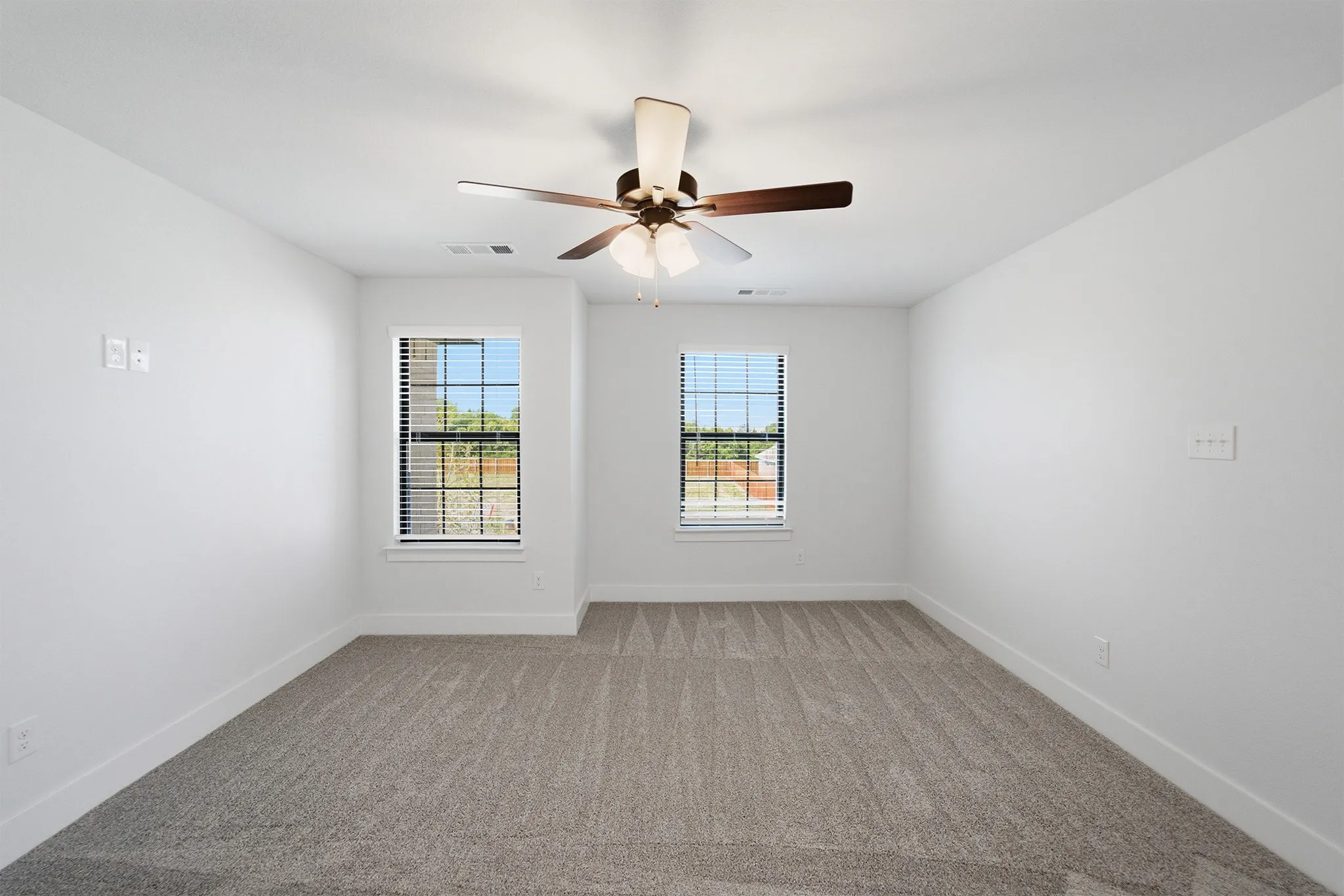 Carpeted room with white walls, dual windows featuring blinds, and a ceiling fan with integrated lighting