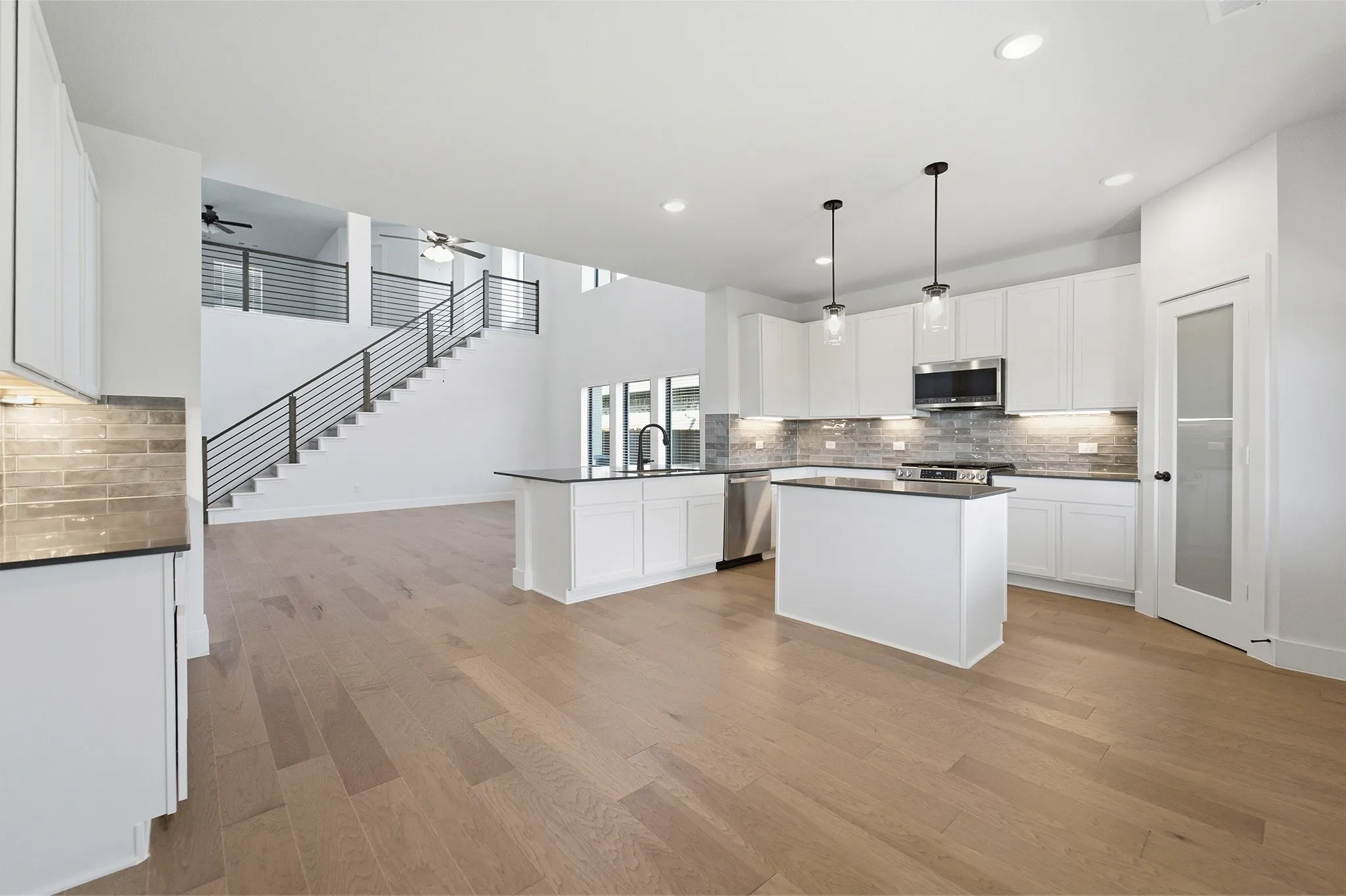 Open-concept living space featuring wood-finish flooring, a contemporary kitchen with white cabinetry, stainless steel appliances, and a tiled backsplash