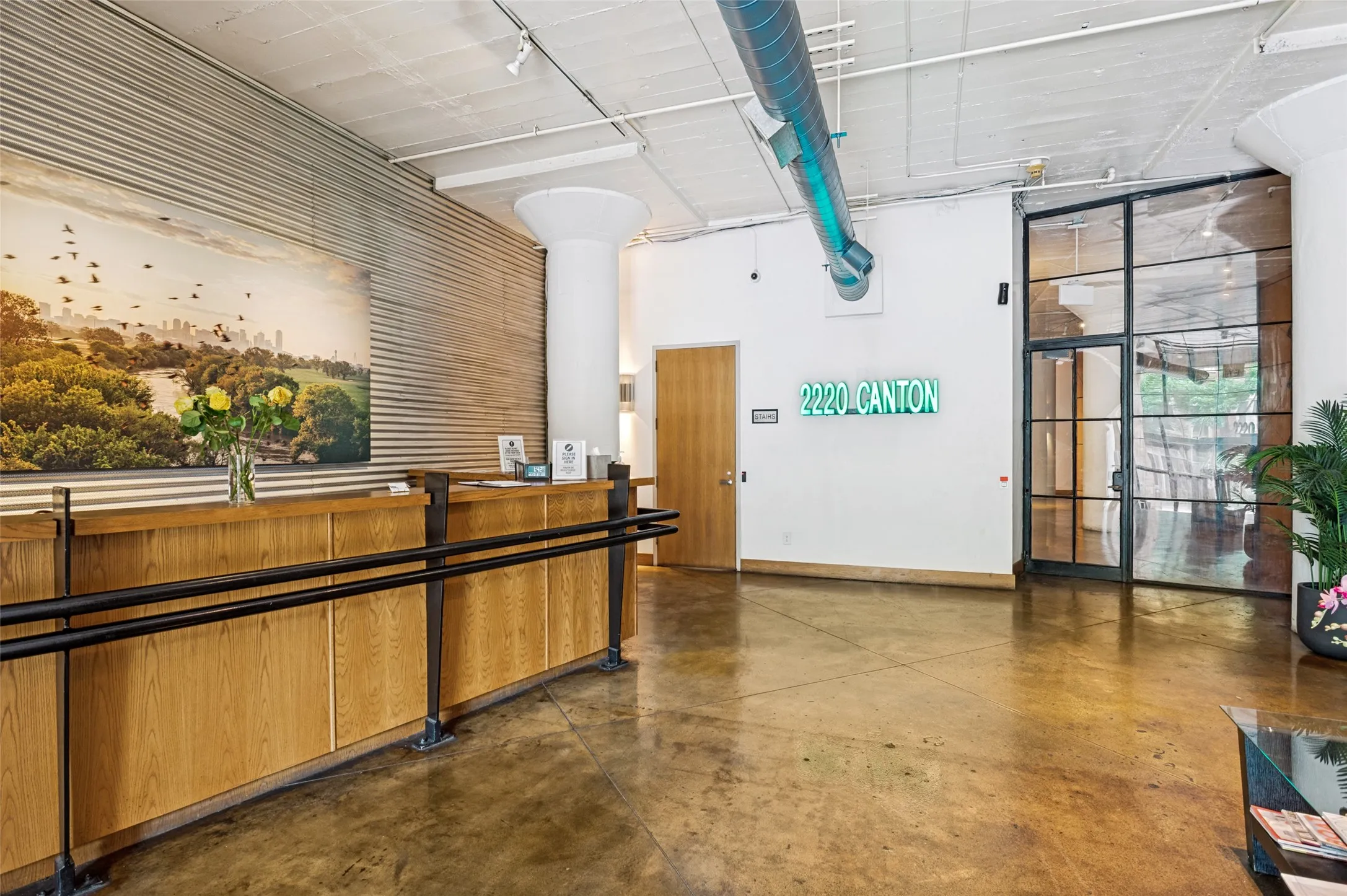 Lobby area featuring polished concrete flooring, exposed overhead ductwork, and a wooden reception desk with black metal railing