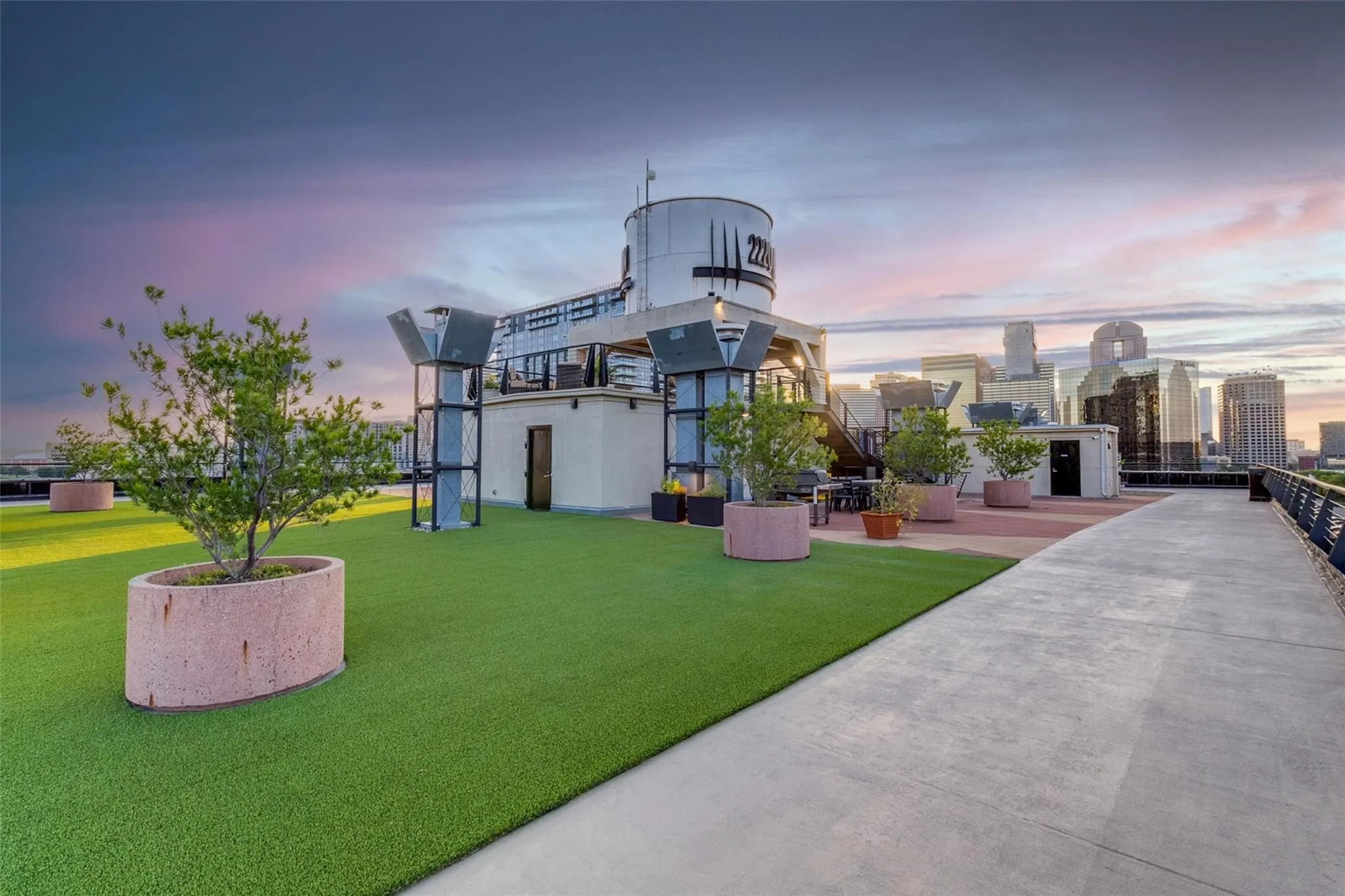 Rooftop amenity space featuring artificial turf, concrete pathways, and multiple planter boxes with mature trees