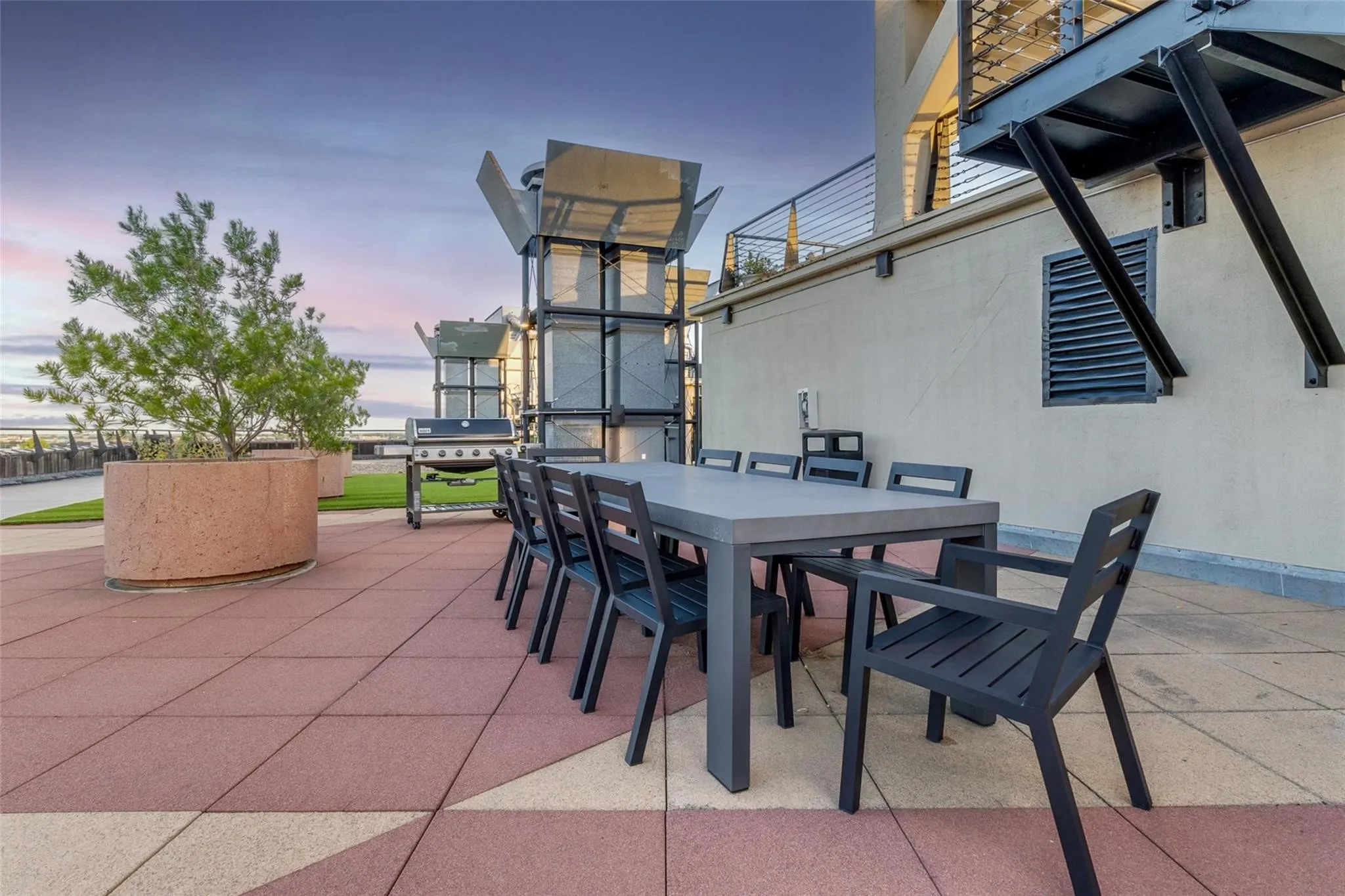 Rooftop patio featuring expansive tiled flooring with geometric patterns, a large rectangular dining table, and a built-in planter with established greenery
